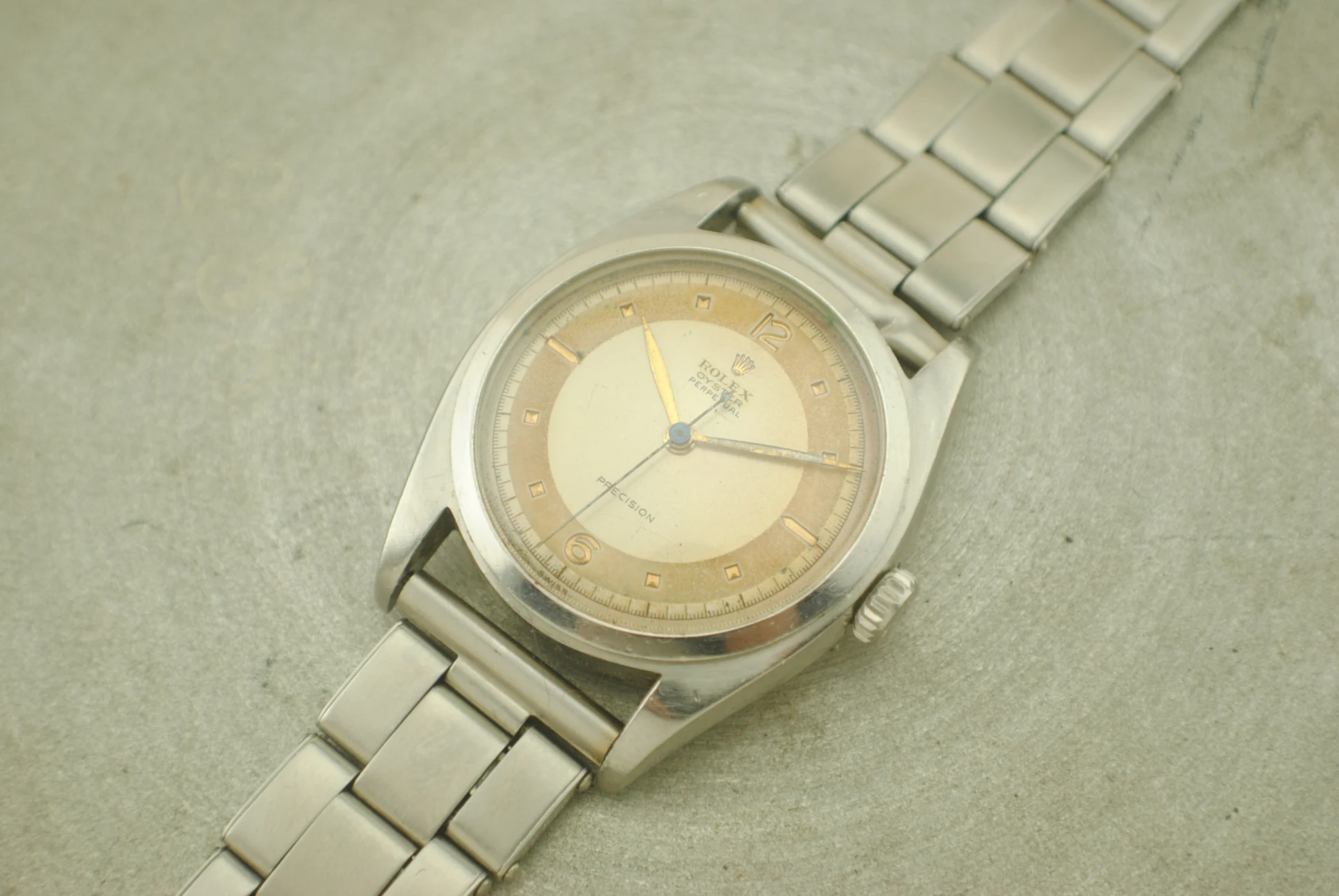 Complete crystal-on Rolex reference 6098 with recessed copper-coloured indexes and riveted straight-end-link bracelet on a grey surface