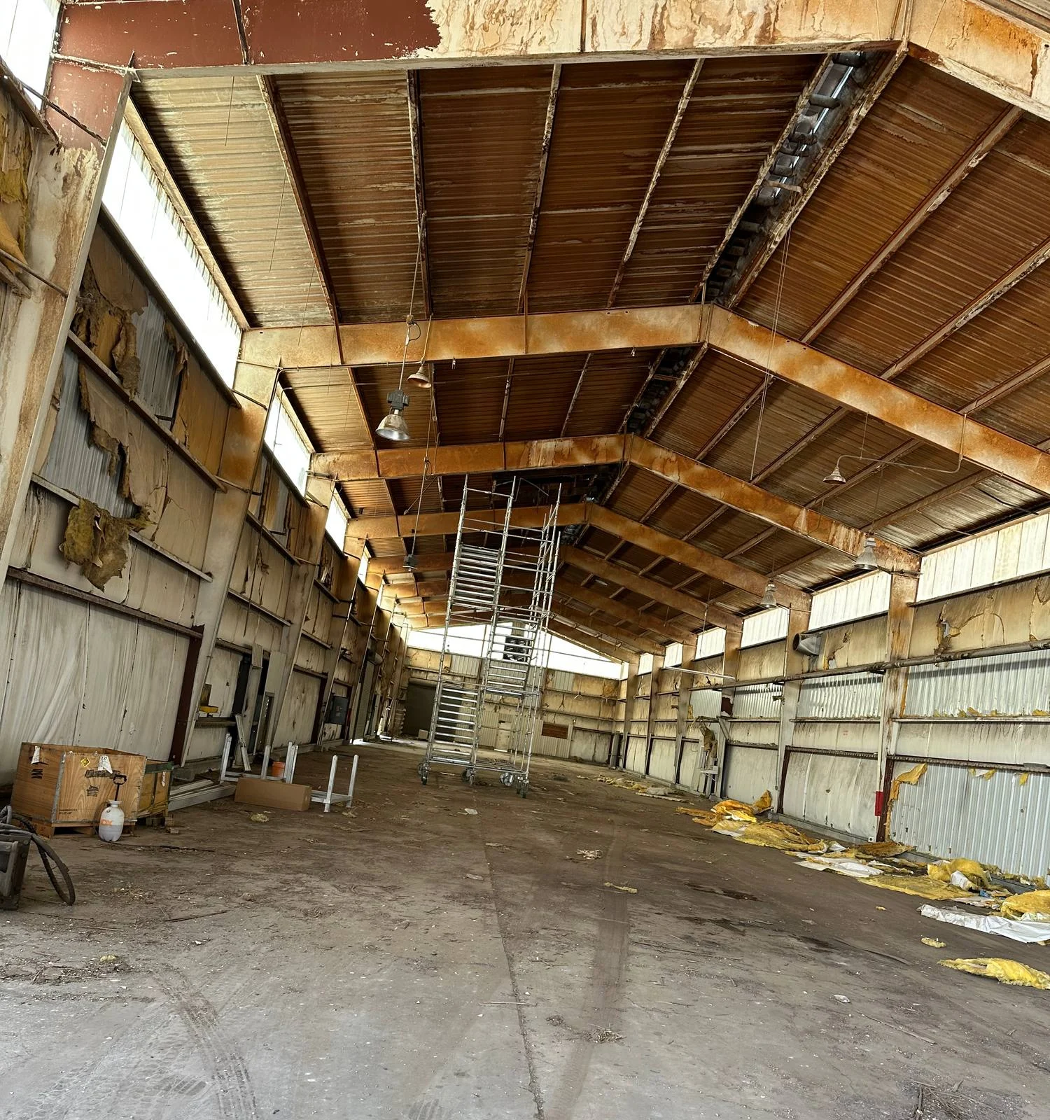 Factory bay with exposed beams and worn insulation before renovation