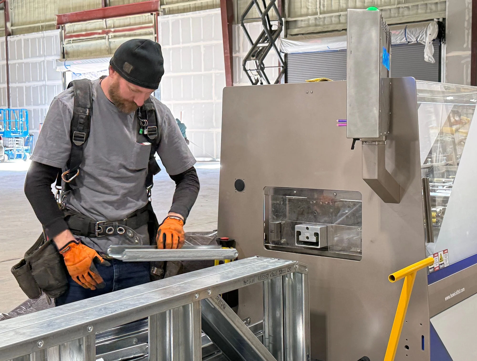 Operator handling a steel member beside a Howick machine