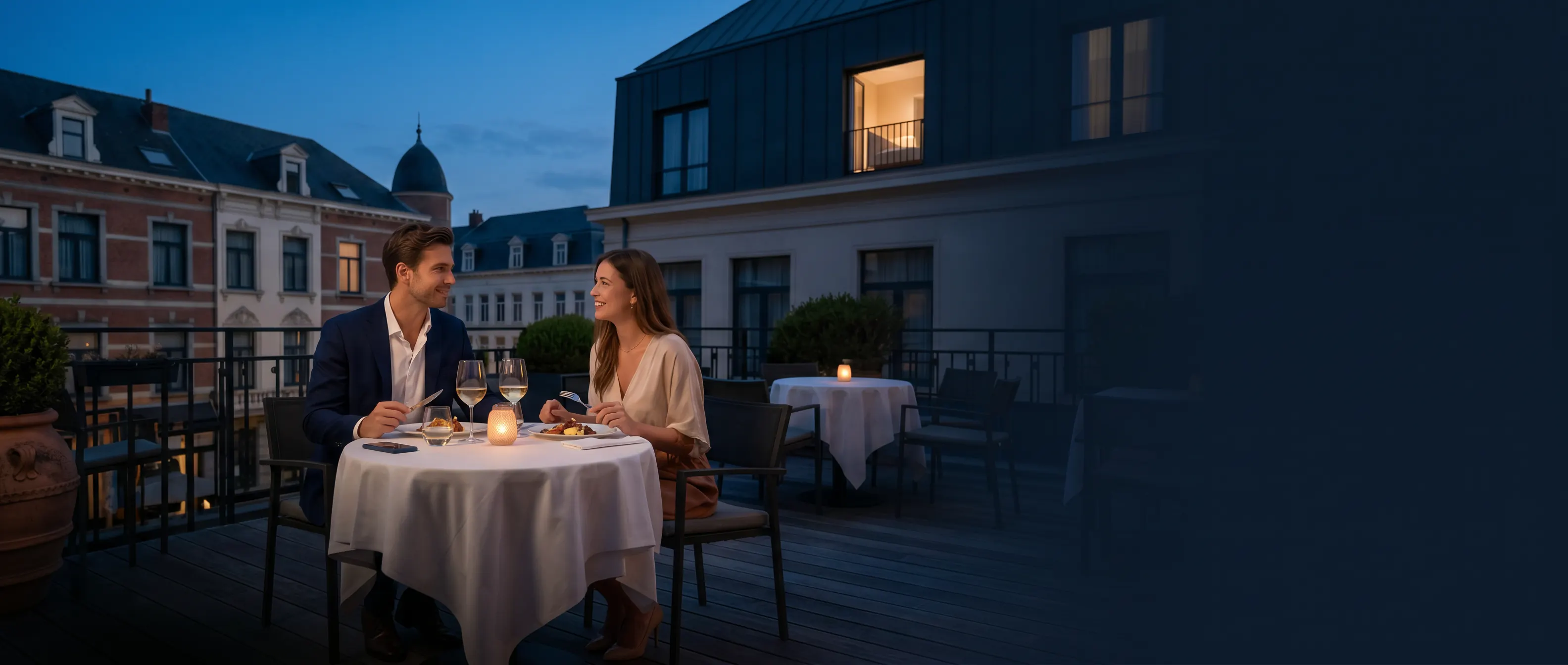 Een jong koppel dineert op het terras van een Europees hotel met een verlichte kamer boven