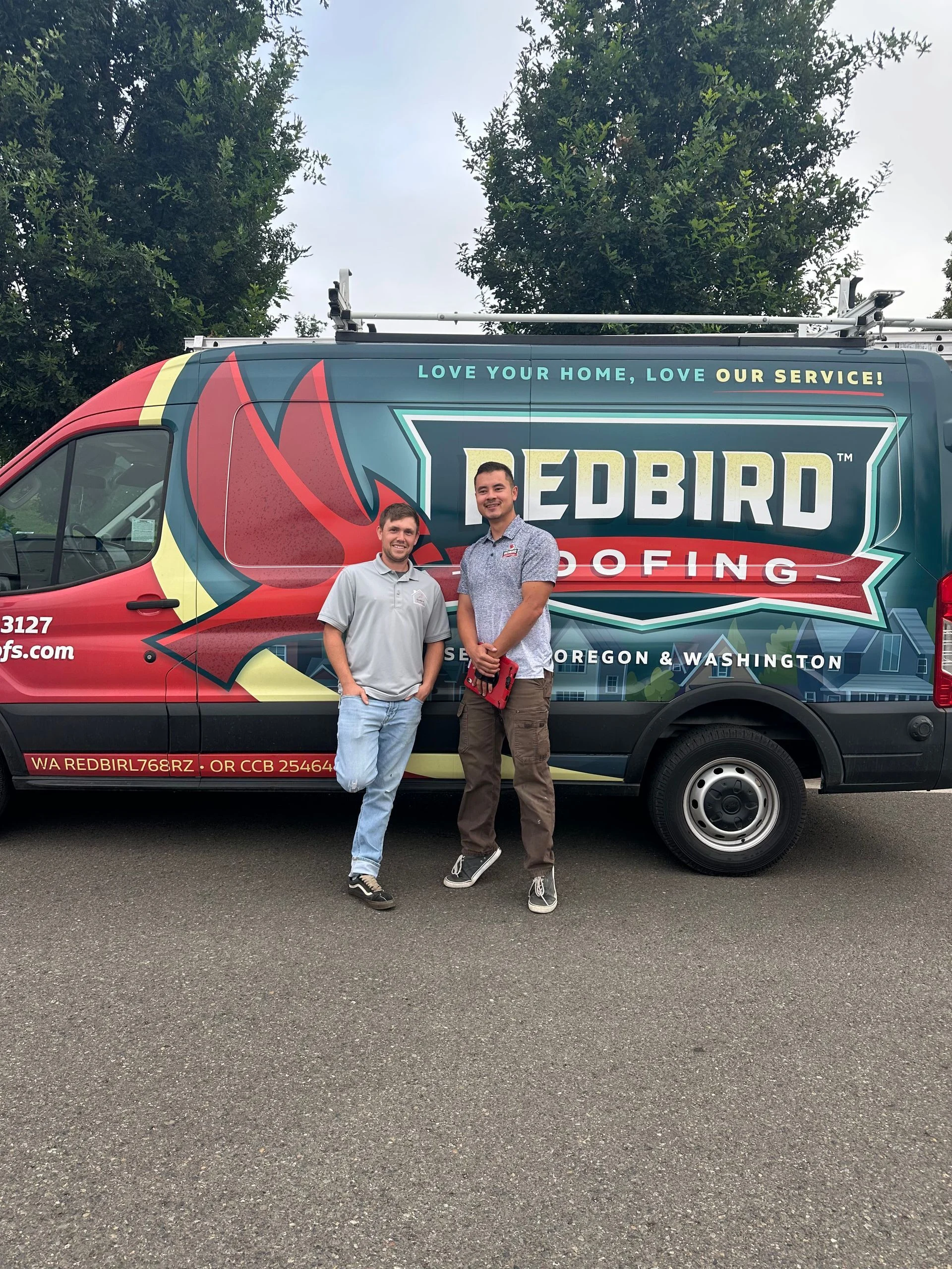 Two people standing in front of a Redbird Roofing branded van in an outdoor, paved area.