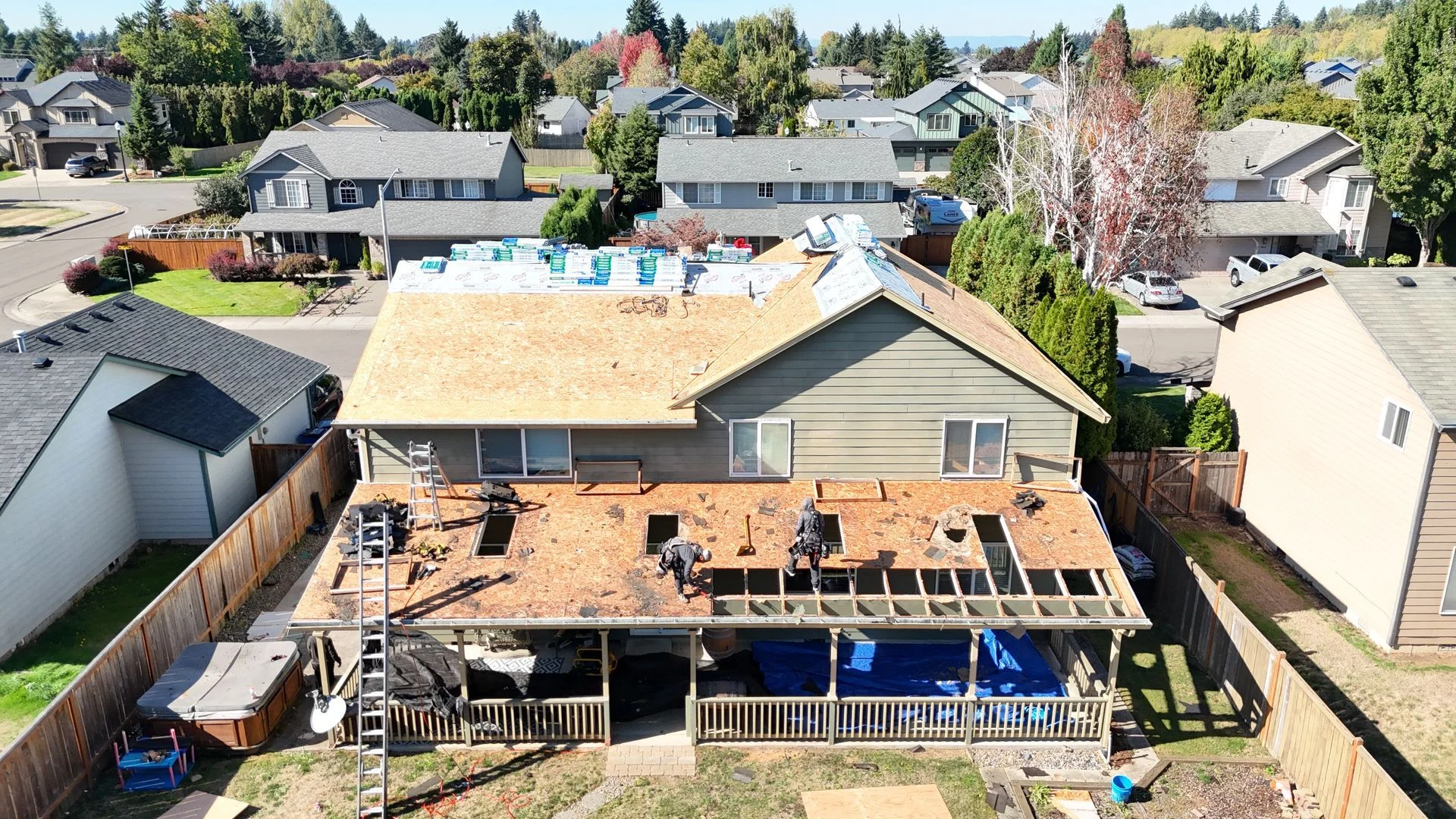 An aerial view shows contractors working on the wooden roof deck of a two-story suburban house during a renovation.