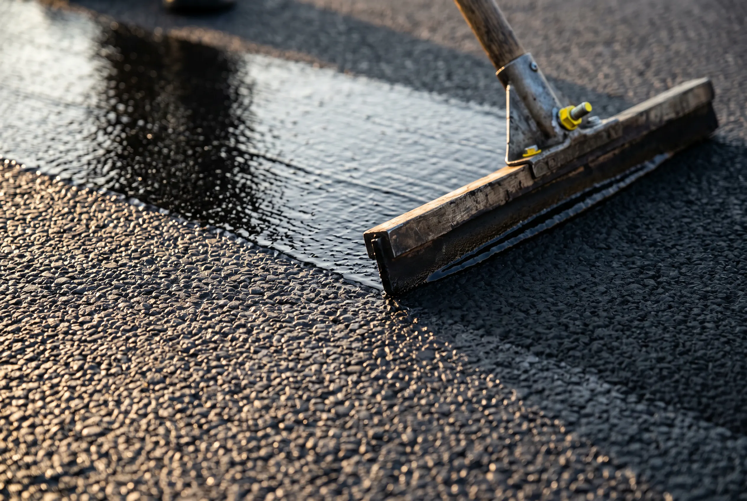 Professional asphalt sealcoat being applied in a smooth pass