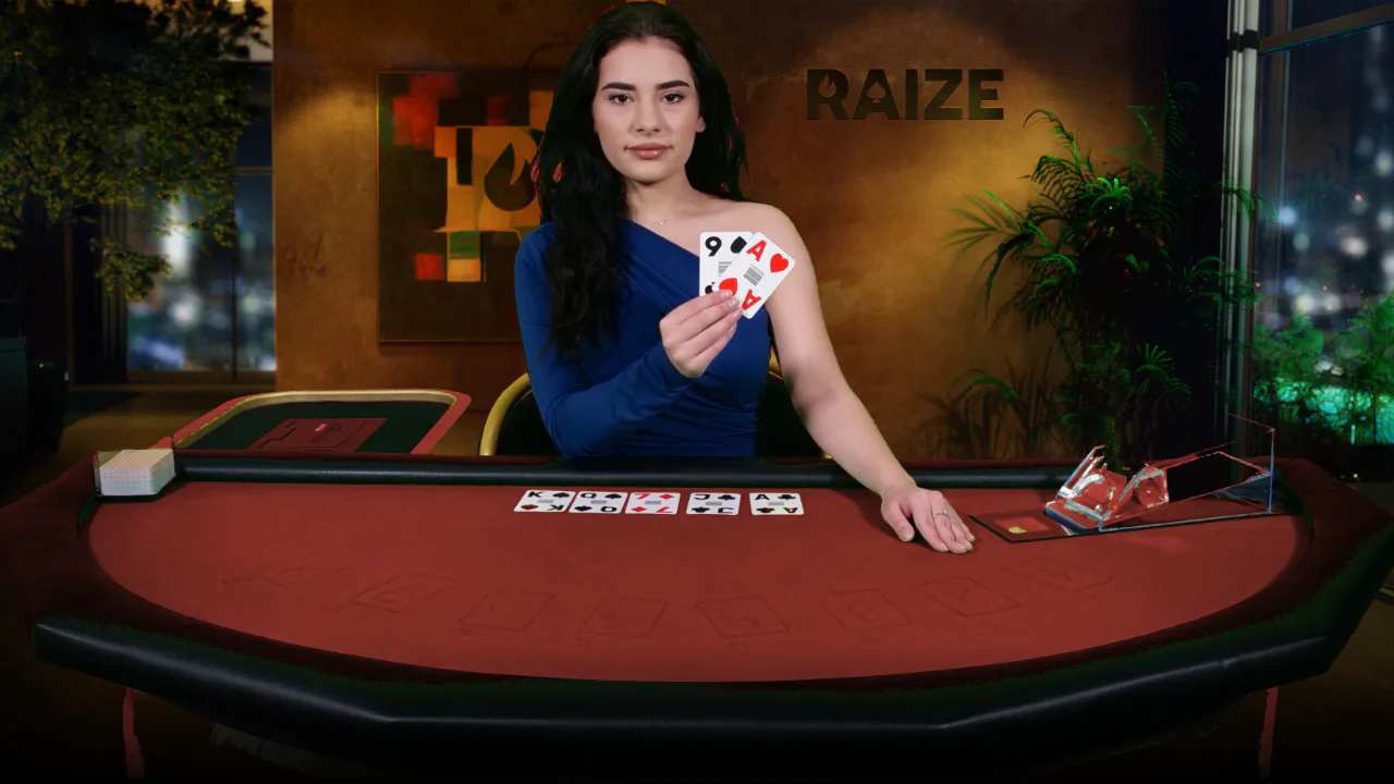 A RAIZE dealer in a blue dress holding up two cards at a red felt table with five community cards dealt
