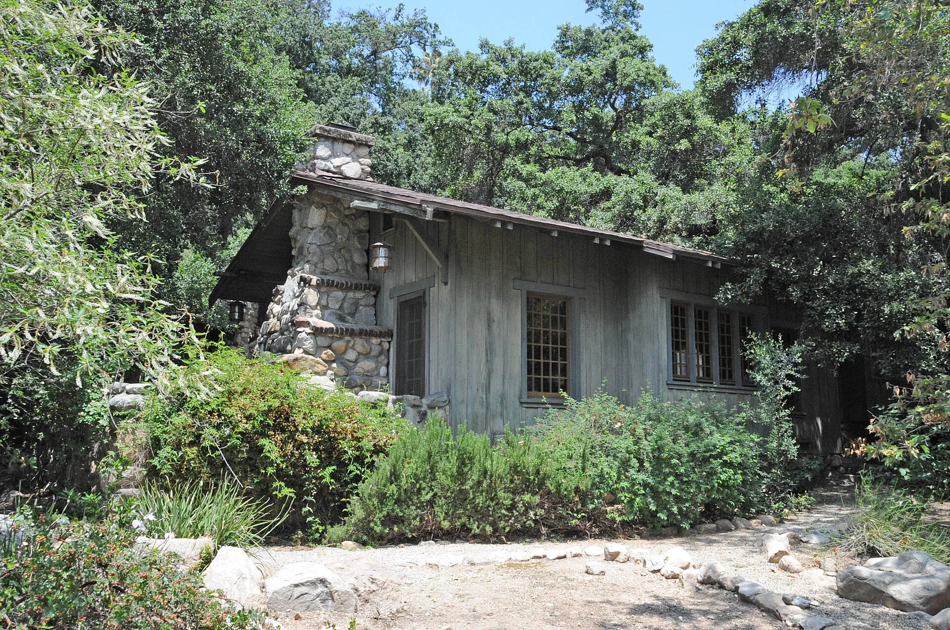 A 1912 Craftsman-style board-and-batten cottage with an arroyo stone chimney among oak trees in Altadena