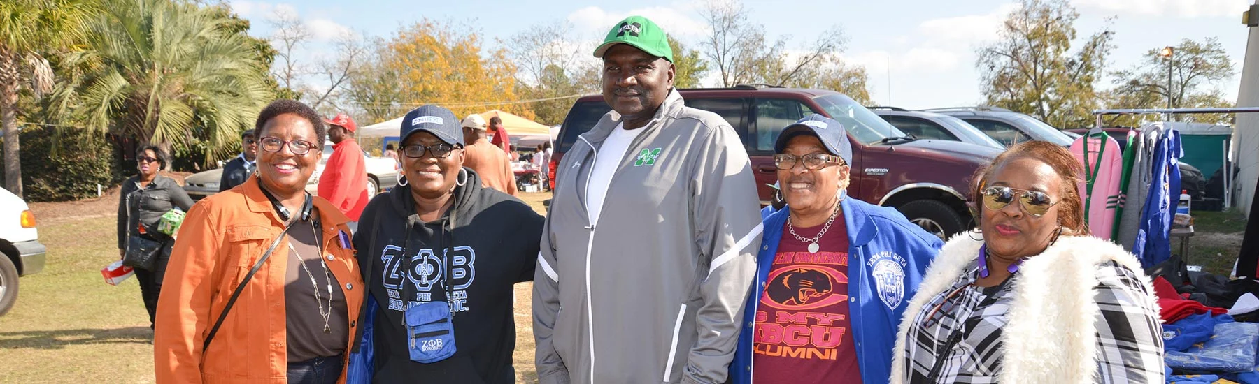 Five Claflin alumni smiling together at an outdoor Homecoming tailgate