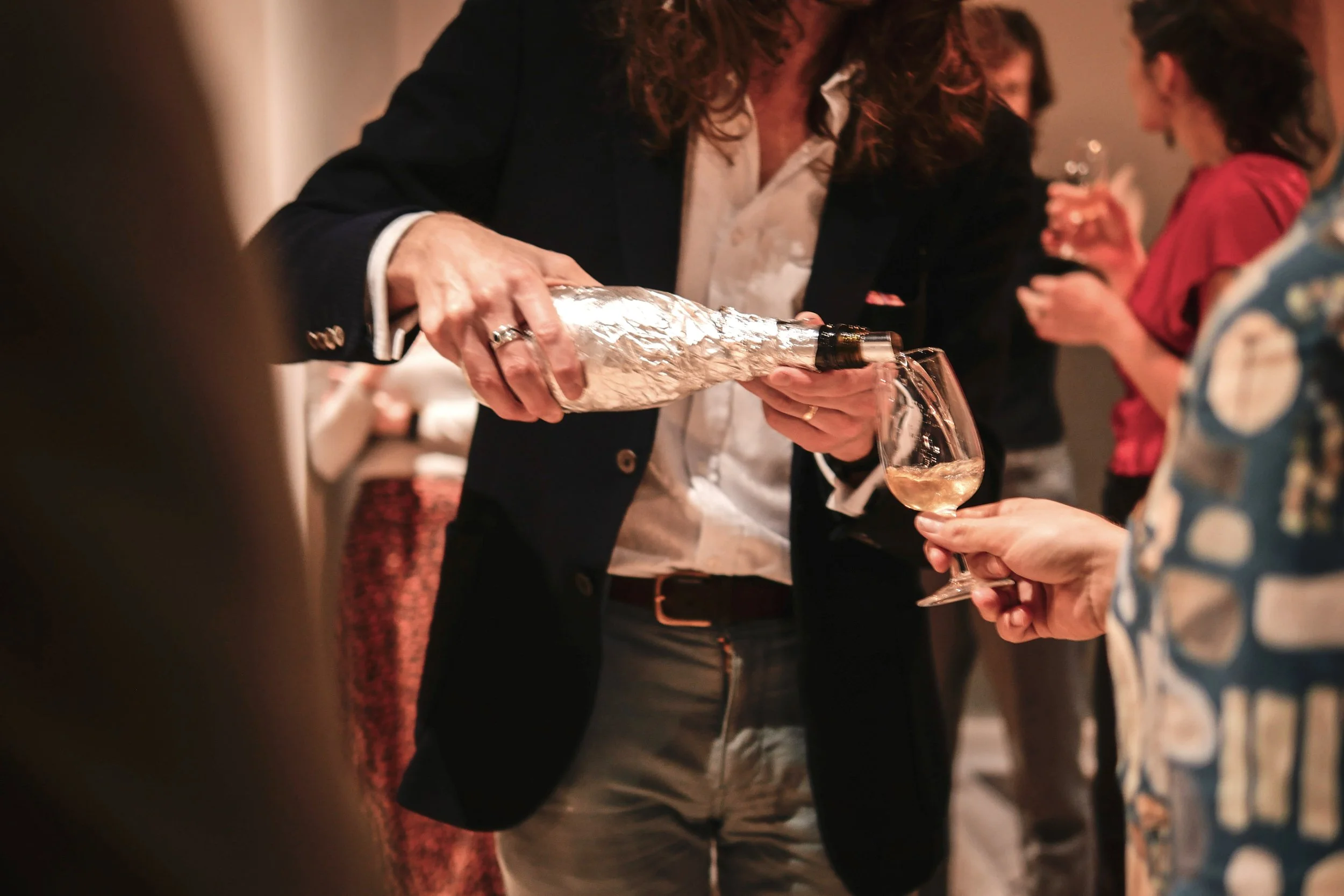 Dr James Flewellen pouring wine from a foil-wrapped bottle for a guest
