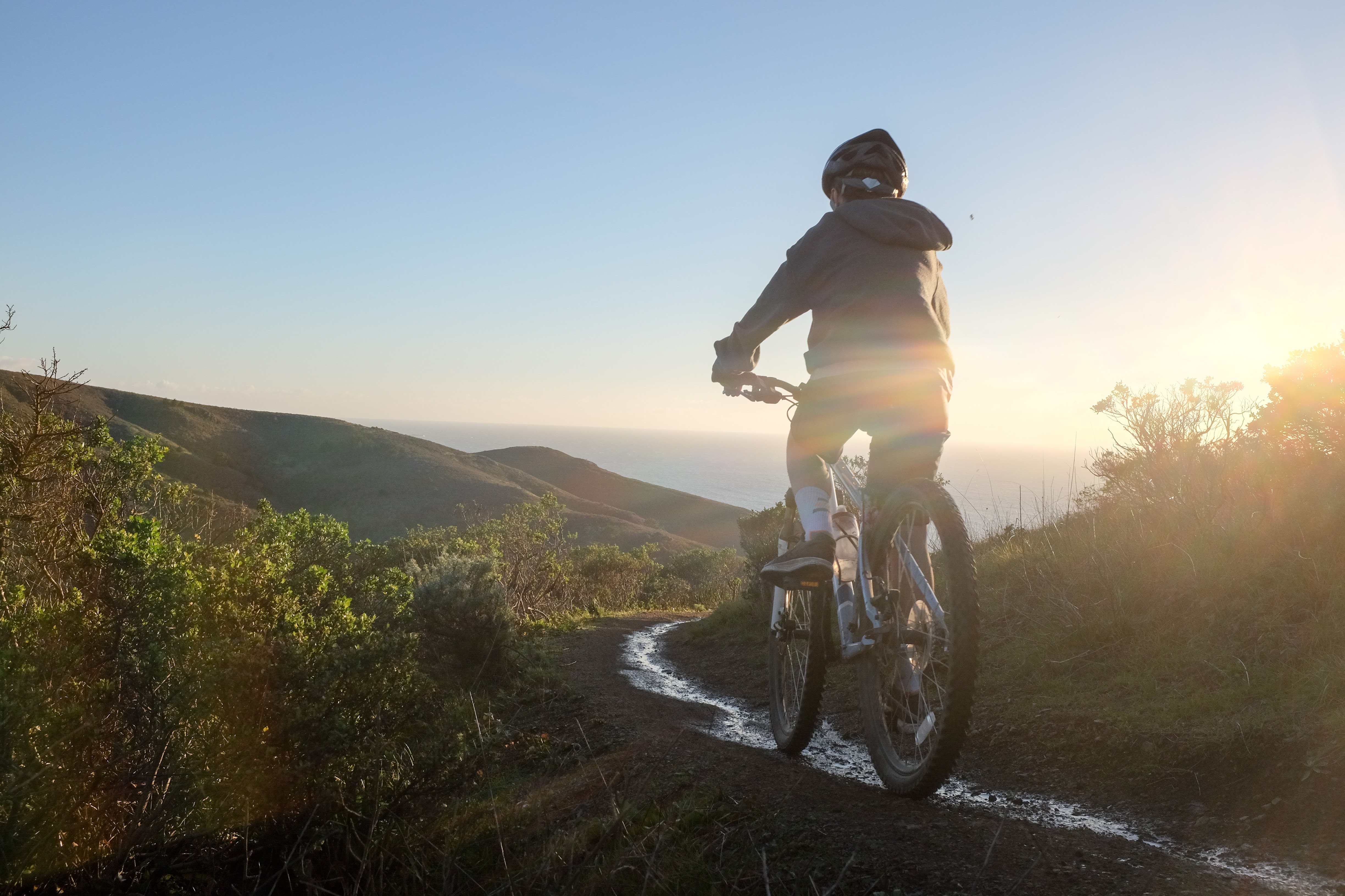 A cyclist riding a coastal Marin trail at golden hour, ocean glowing behind the ridgeline.