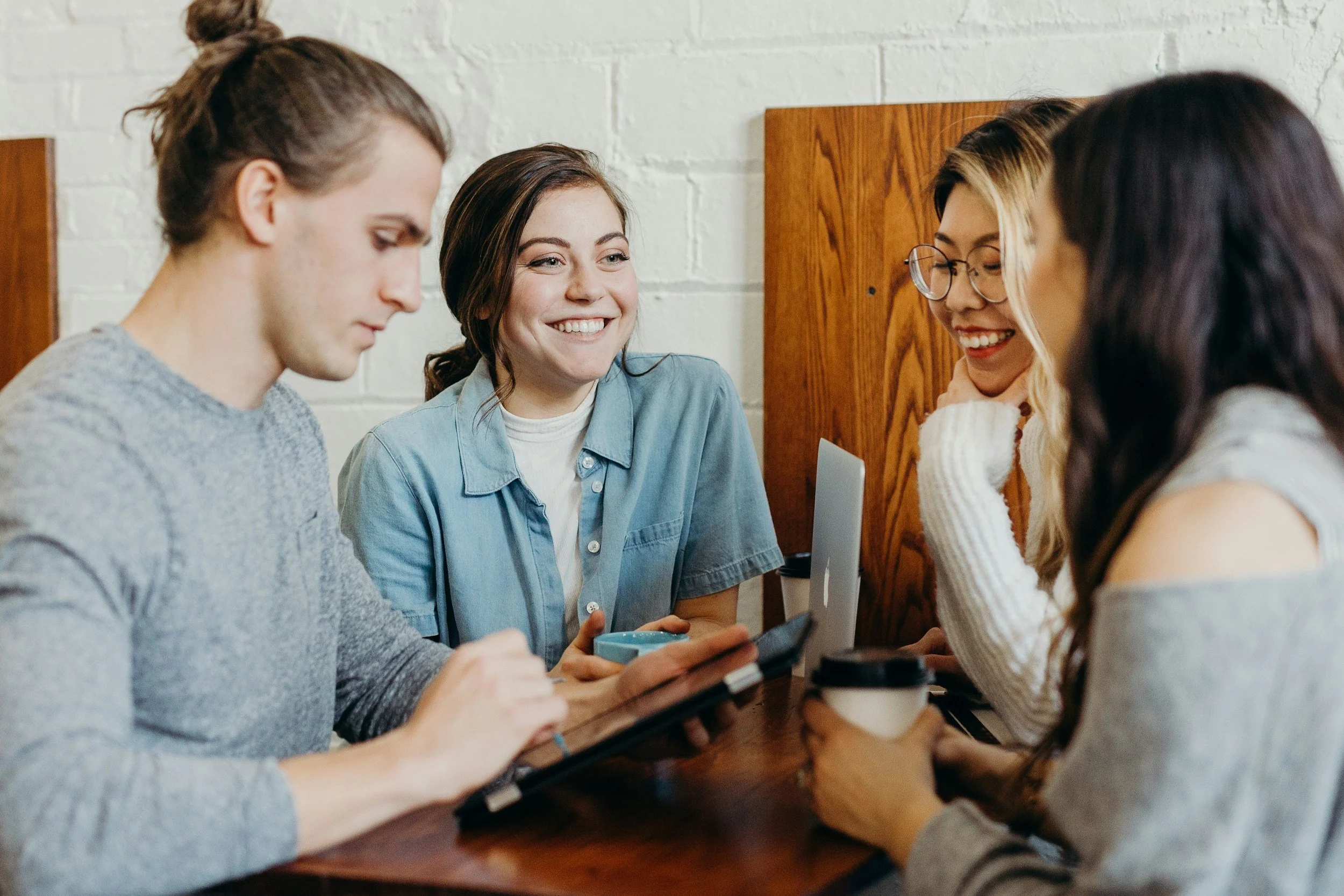 A group of professionals sitting together at a wooden table, looking at a digital tablet.