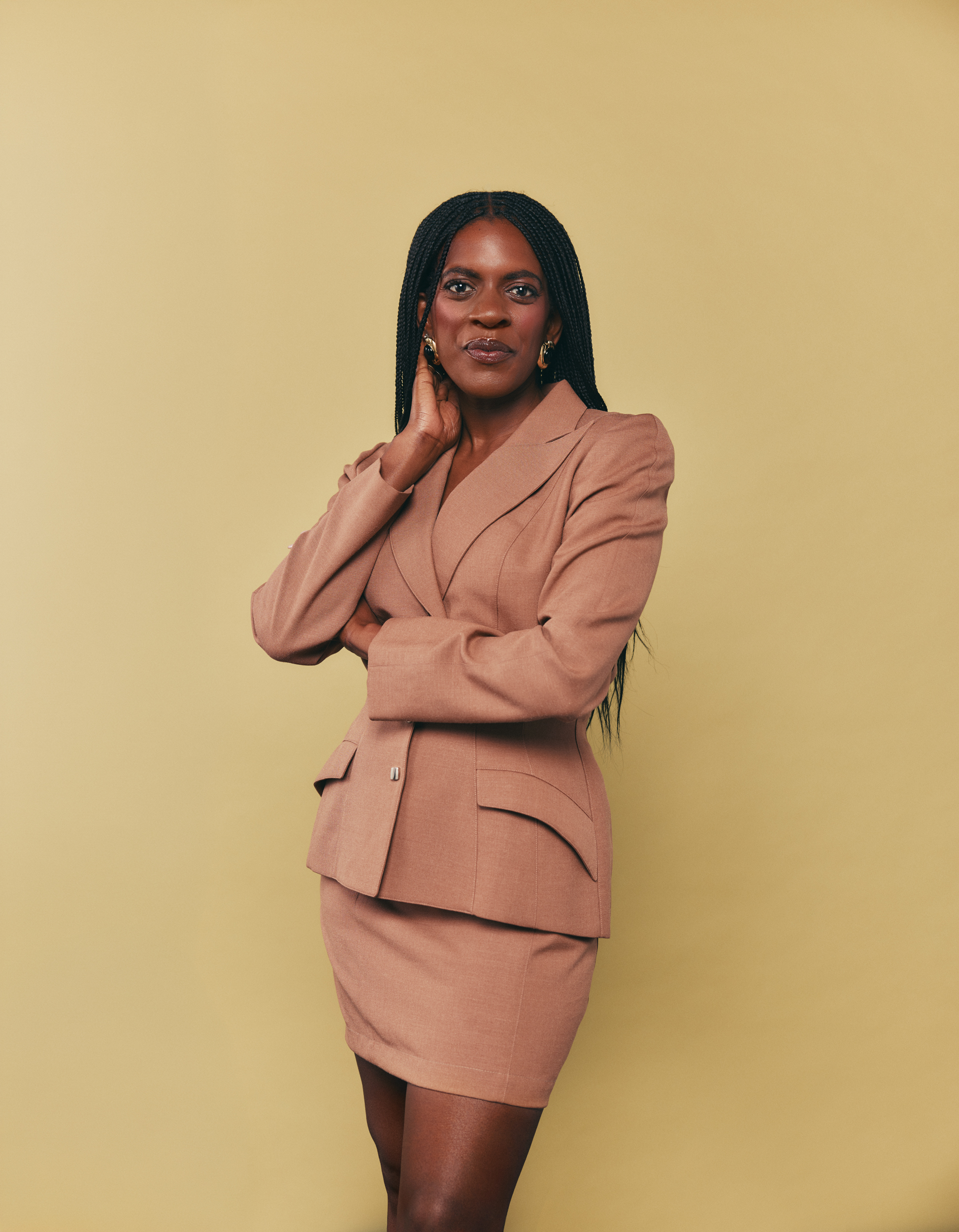 Ashley Rudolph, executive and performance coach, in a tailored camel suit against a warm studio backdrop.