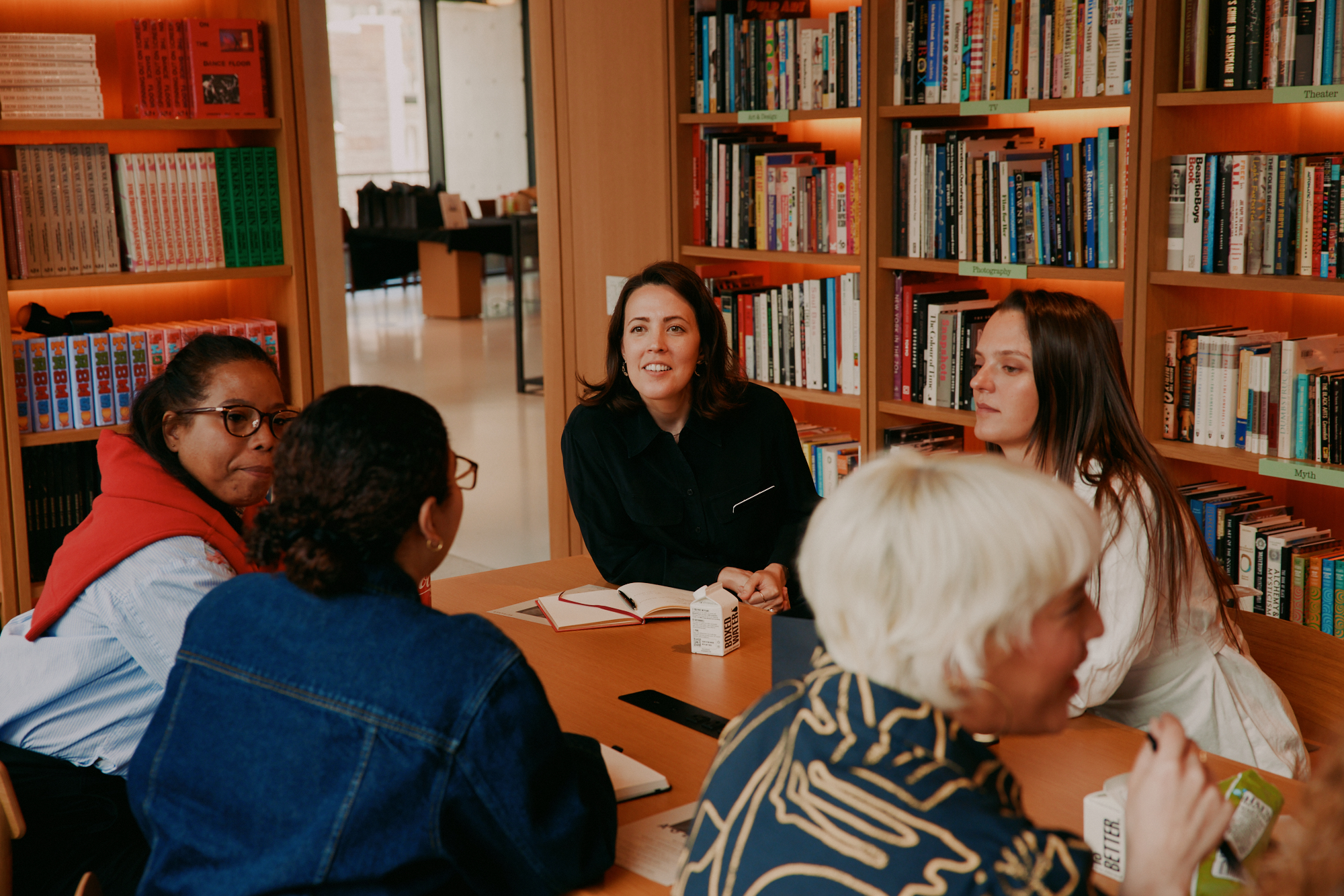 Ashley Rudolph leading a small group coaching session around a table in a warm, book-lined room.