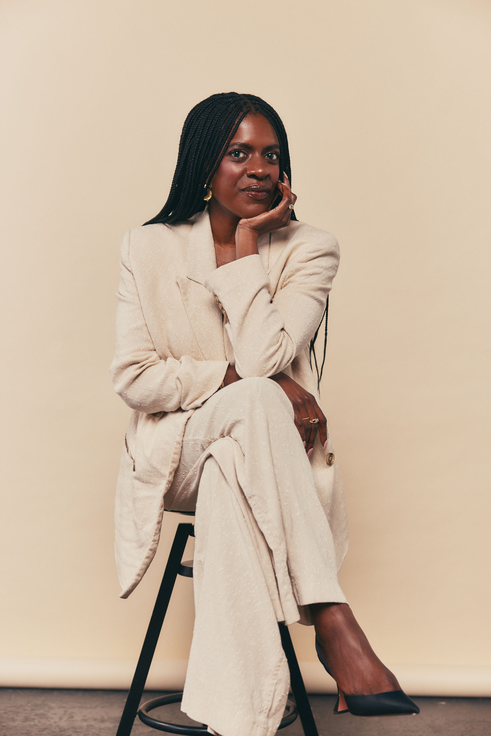 Ashley Rudolph, executive and performance coach, seated on a stool against a warm cream studio backdrop.
