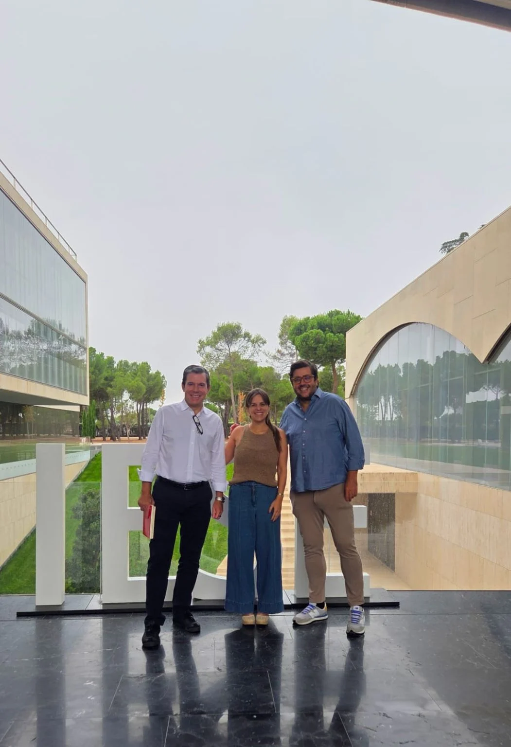 Tres participantes de una mentoría de WeGrow posan junto a las letras de IESE en el campus.