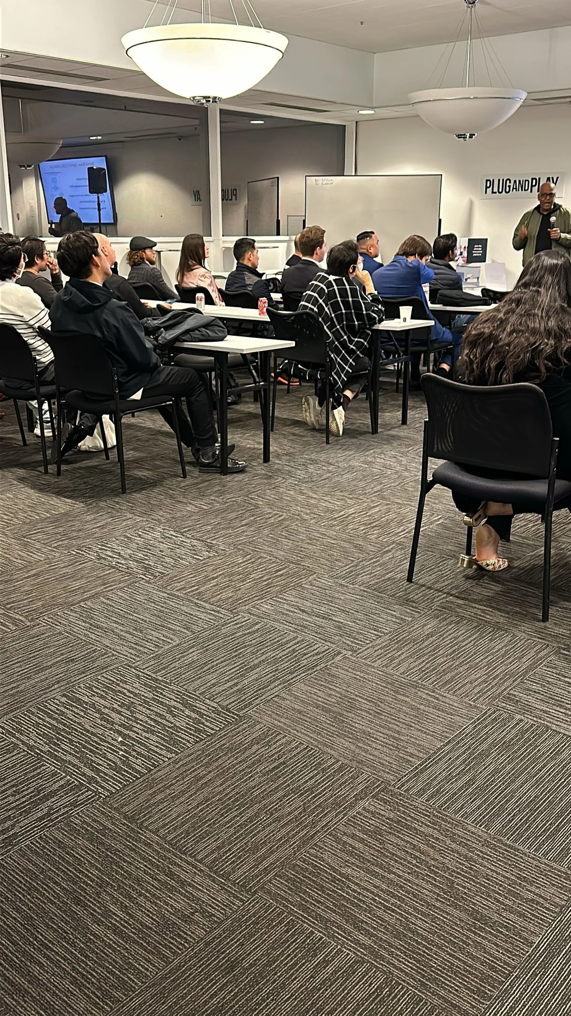 Seated audience facing a speaker holding a microphone.