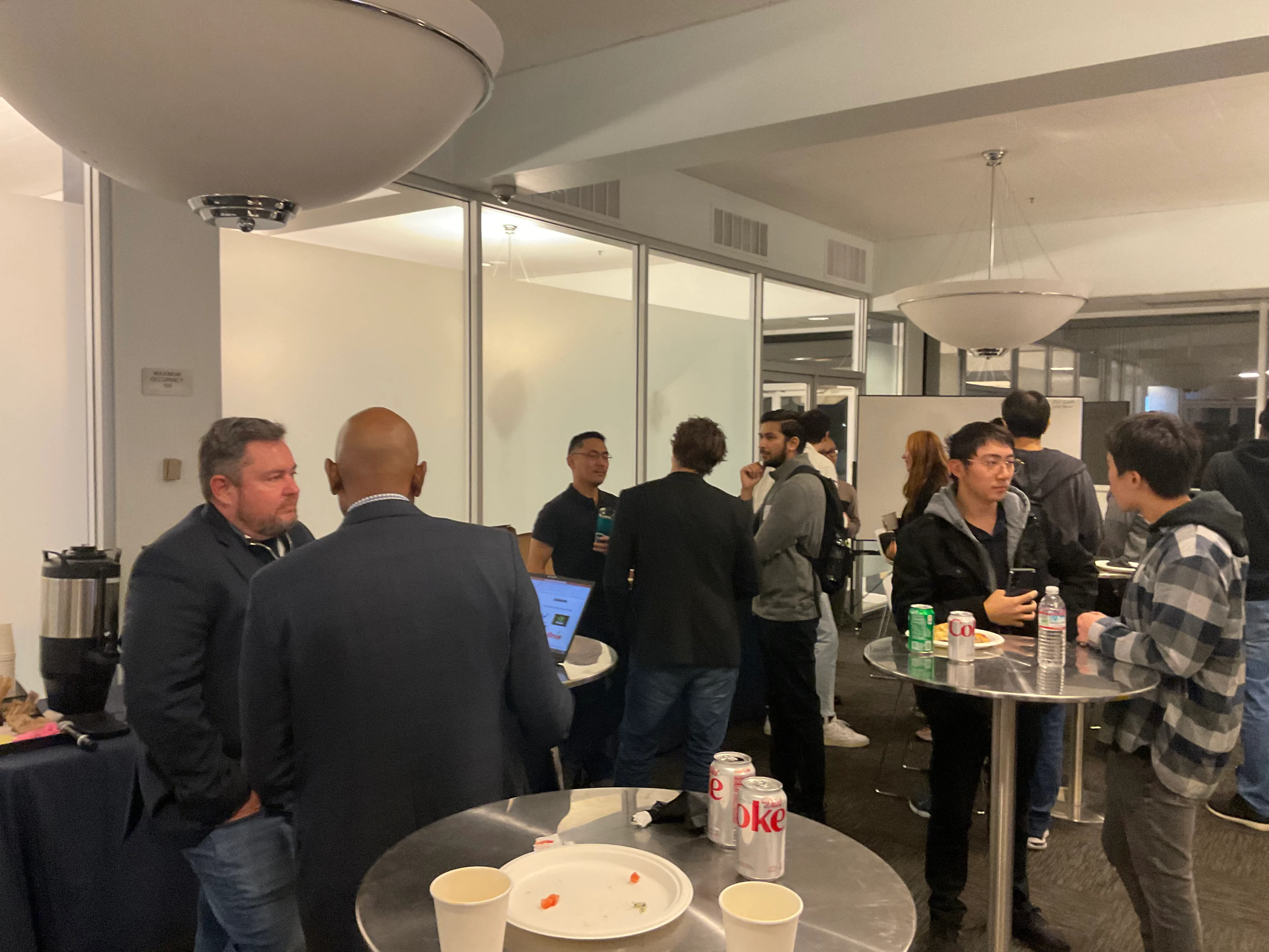 Small groups talking beside high tables and refreshments.