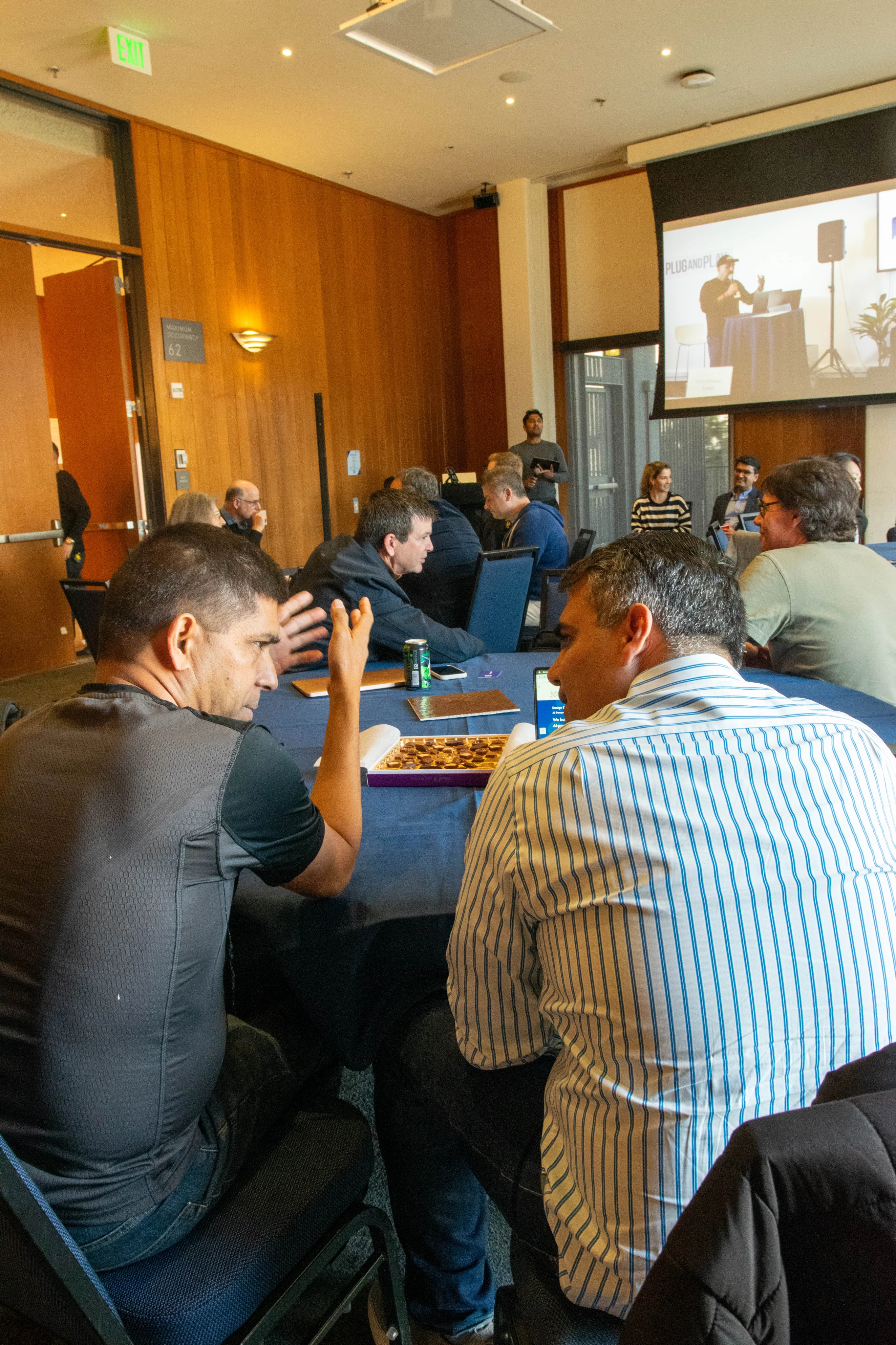 Attendees talking across a round table beneath a projection screen.