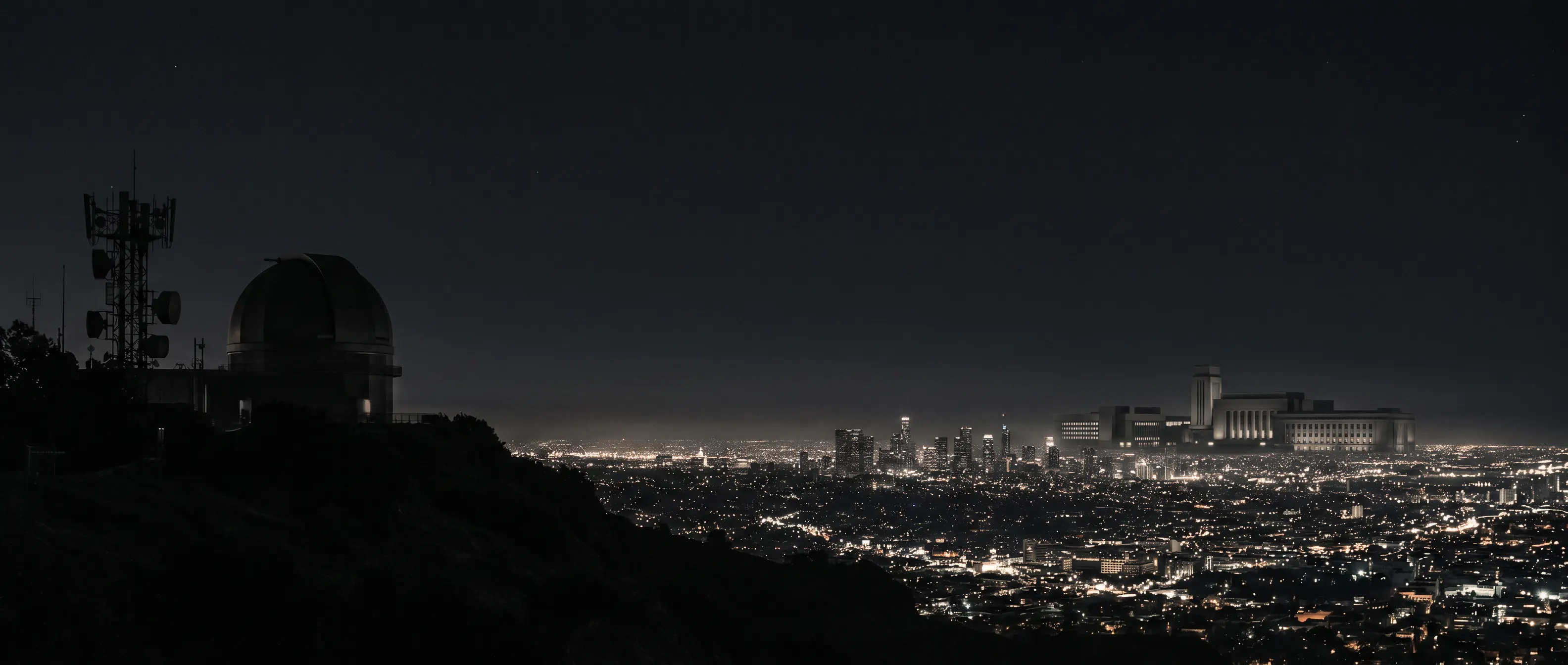 A dark observatory ridge overlooking a vast illuminated city and institutional skyline