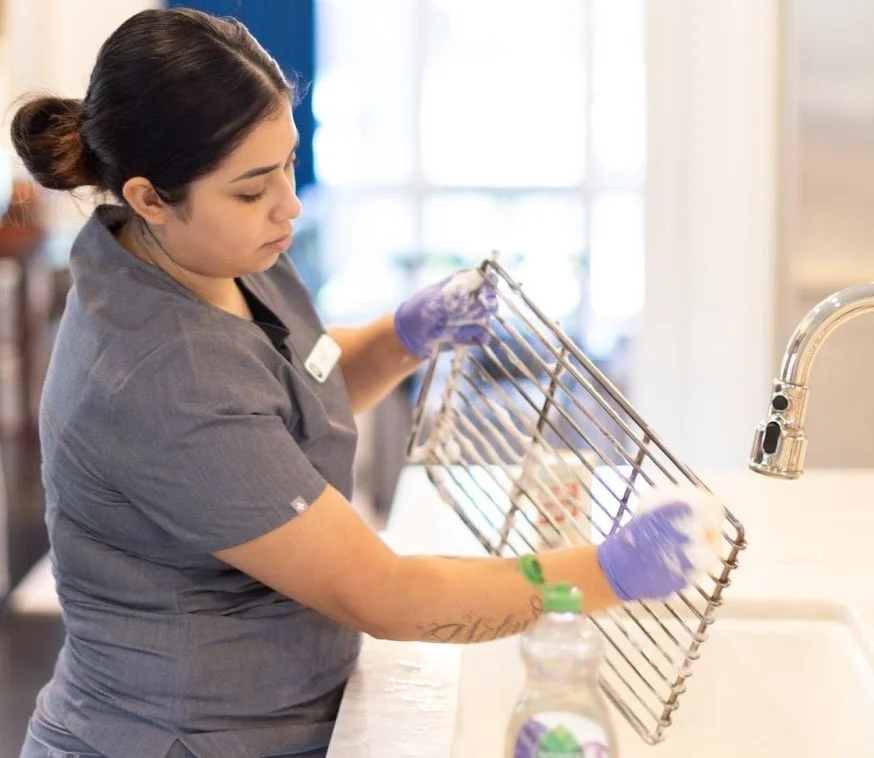 A professional cleaner wearing gloves is scrubbing a metal rack over a sink