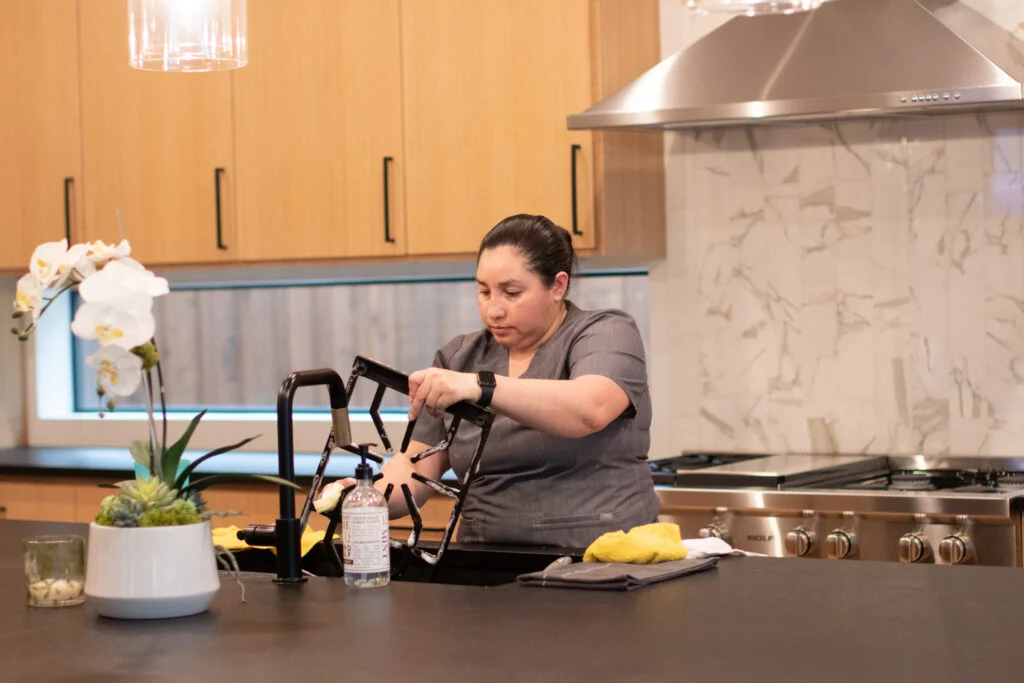 Professional cleaner sanitizing a kitchen faucet in a modern kitchen.