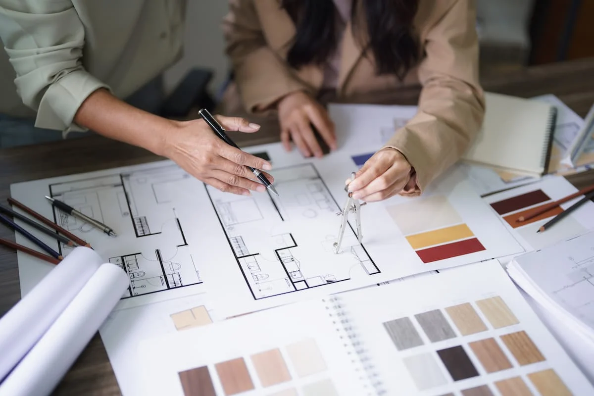 Two people reviewing a residential floor plan and finish samples at a worktable
