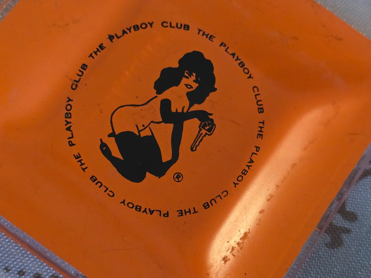 מאפרת זכוכית כתומה וינטג' "The Playboy Club", הדפס דמות ארנבונת המחזיקה מפתח – פריט אספנות רטרו מידות: 9.5 x 9.5 ס"מ