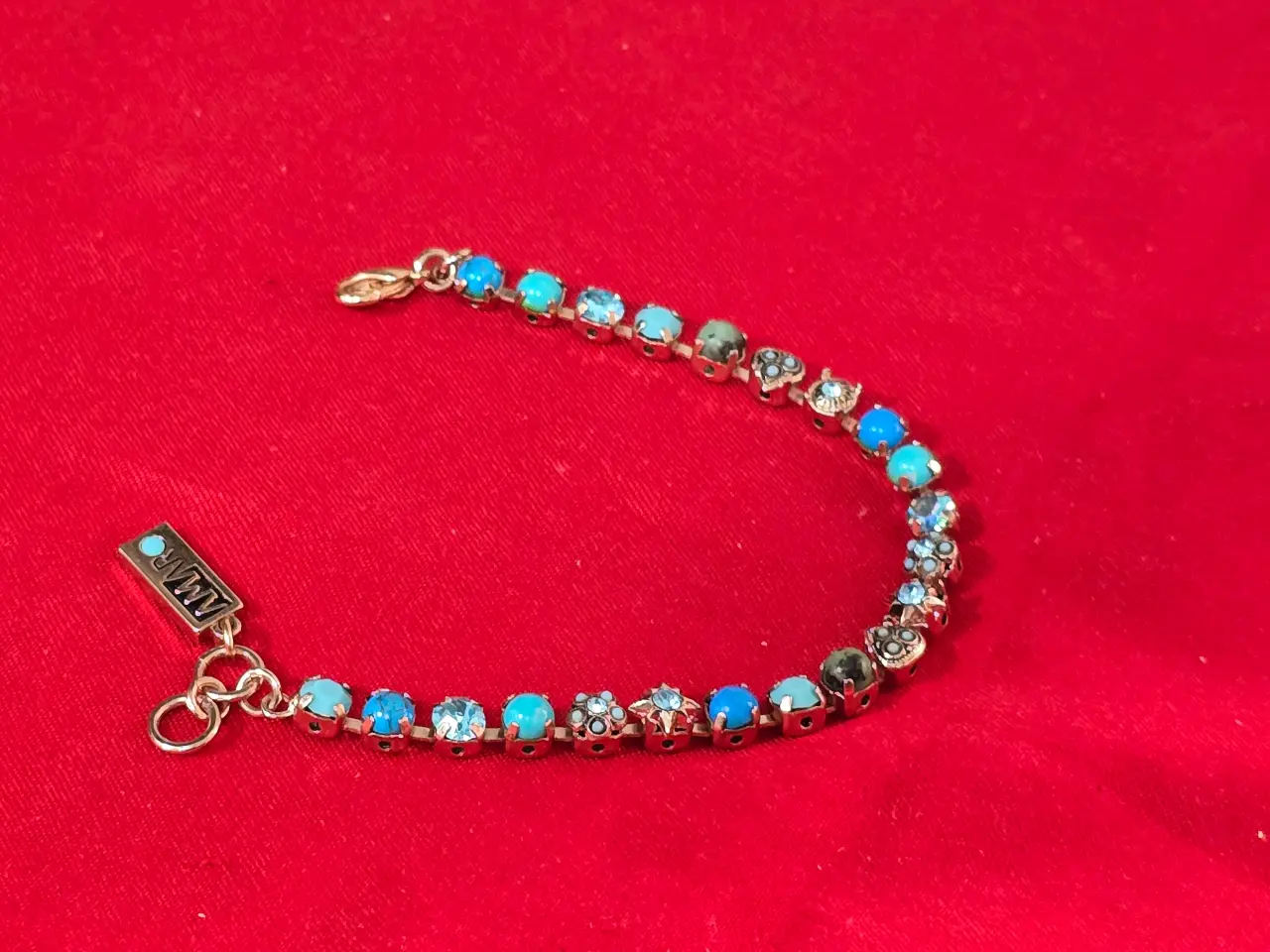 צמיד טניס וינט'ג של המותג אמארו (Amaro) עשוי מפליז בגימור מוזהב ומשובץ באבני תורכיז וקריסטלים בגווני  כחול ותכלת