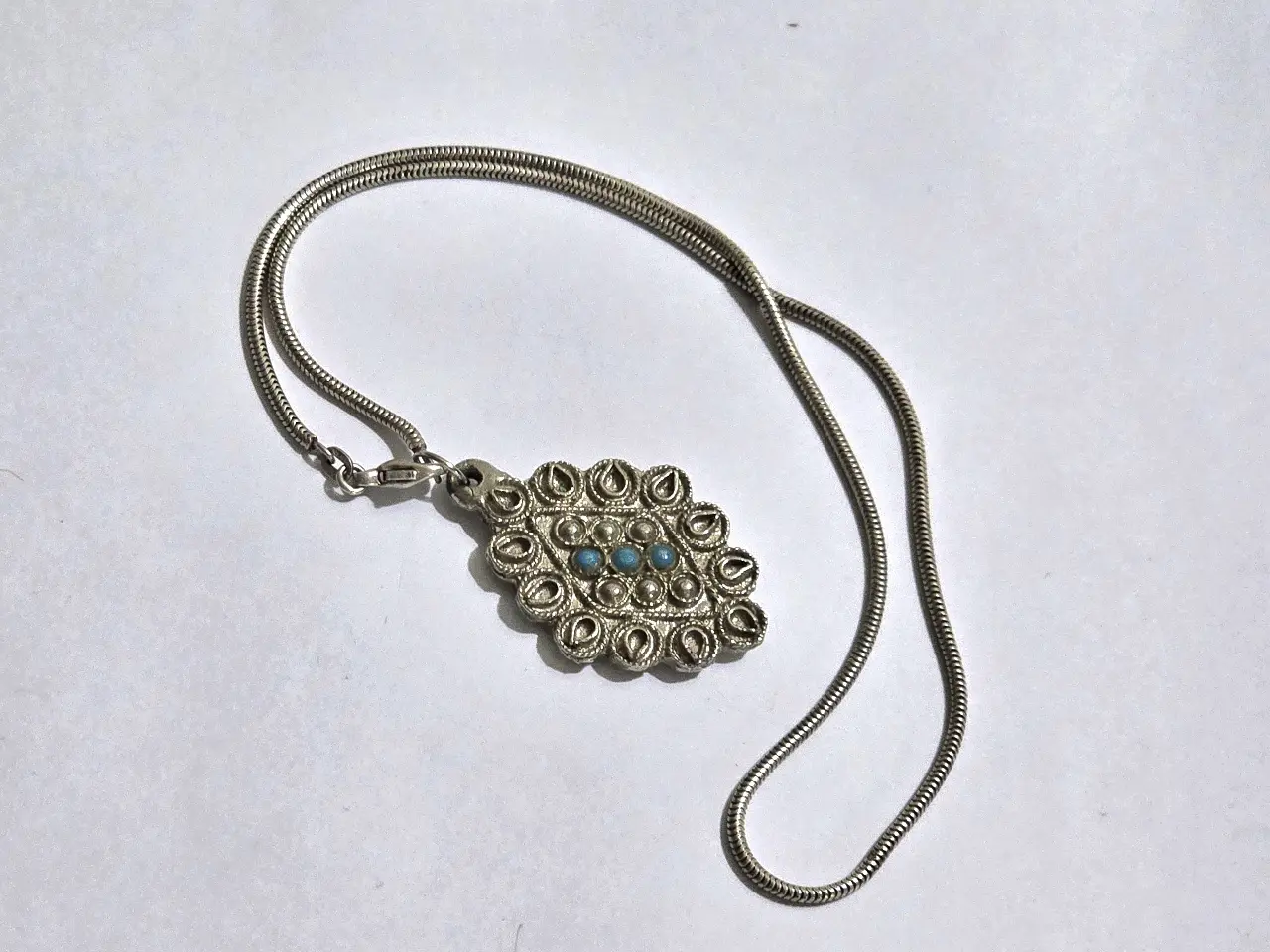 תכשיט יודאיקה. שרשרת כסף סטרלינג. חתומה 925. עם תליון. בצד אחד שלו יש תבליט של ספר תורה, עם מגן דוד, כתר תורה ולוחות הברית וכן הכיתוב ירושלים. בצד השני יש אבני טורקיז. אורך: 40 ס"מ. התליון: 4 ס"מ.