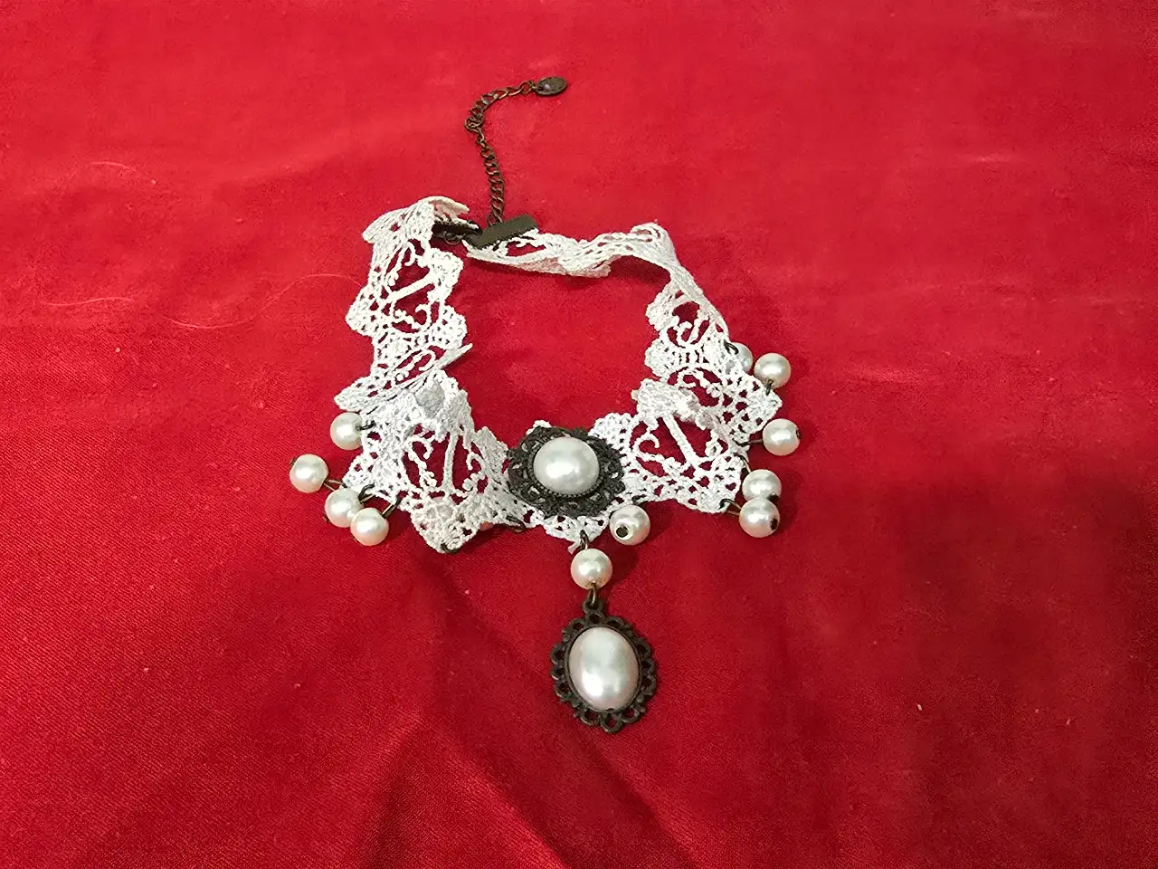 זוג שרשראות צ'וקר צמודות לצוואר שנהם מתחרה סגנון ויקטוריאני או גותי השרשרת הלבנה עשויה מתחרה לבנה בדוגמא גאומטרית שבחלק התחתון פנינים קטנות על גבי לולאות מתכת דקיקות התליון המרכזי משובץ בפנינה גדולה מעוטרת בהברונזה הצו'קר השחור מתחרה בדוגמת רשת עם סוגר ושרשרת הארכה כסוף