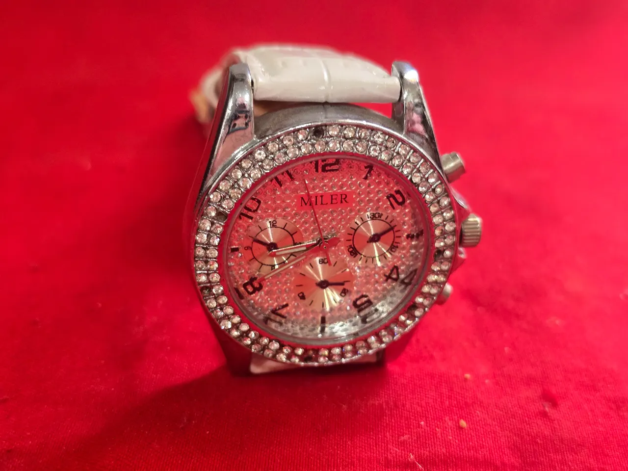 שעון יד חדש לגמרי הלוח מעוטר בשיבוץ צפוף של אבנים קטנות השעון עשוי ממתכת בגוון כסף רצועת עור לבנה דמוי עור תנין