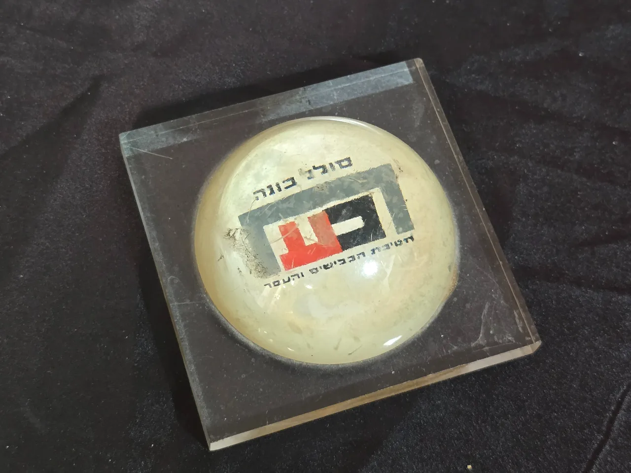 משקולת נייר שהיא גם פרסומת  סולל בונה  חטיבת הכבישים והעפר . תוצרת הצבי -  קיבוץ מעיין צבי . שריטות ...  מידה 9.5 על 9.5 על 4 סמ