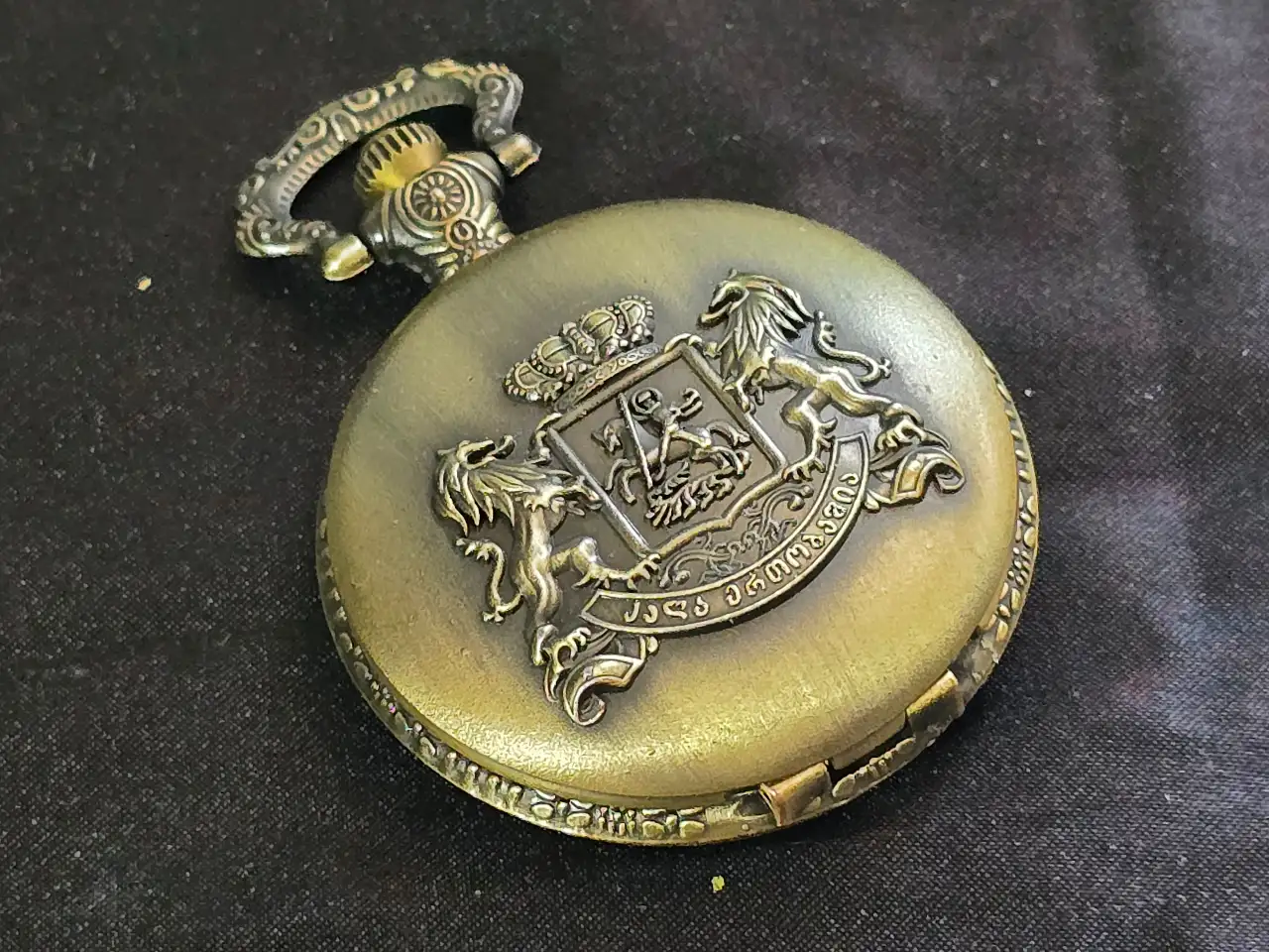 שעון כיס עם תבליט סמל מדינת גאורגיה, מצב עבודה תקין, עם מחוג שניות. מנגנון קוורץ, לוח השעון בגוון לבן. הקופסה עשויה מתכת בגוון ברונזה, פתיחה באמצעות לחיצה על הכפתור. קוטר - 46 מ"מ מצב מושלם.