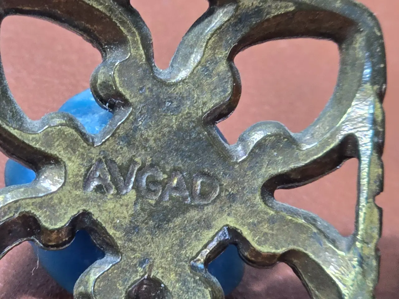 תליון מתכת כנראה ברונזה במרכזו שושנה כחולה התליוןל של ח'ב אבגד חברה ישראלית מידות 3.5*3