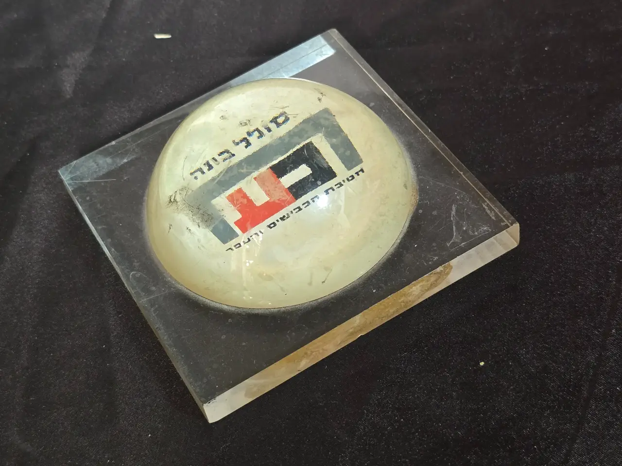 משקולת נייר שהיא גם פרסומת  סולל בונה  חטיבת הכבישים והעפר . תוצרת הצבי -  קיבוץ מעיין צבי . שריטות ...  מידה 9.5 על 9.5 על 4 סמ
