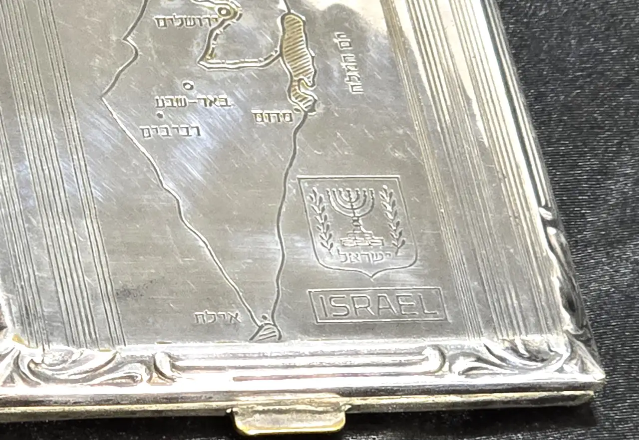 קופסת סיגריות עם מפת ישראל. ככל הנראה מתכת מצופה כסף. מדבקות מס קנייה. אמצע המאה העשרים בקירוב. 8X9 ס"מ על הקופסה מופיעות המילים ישראל בעיברית ואנגלית ושמות הערים הגדולות בארץ ישראל
