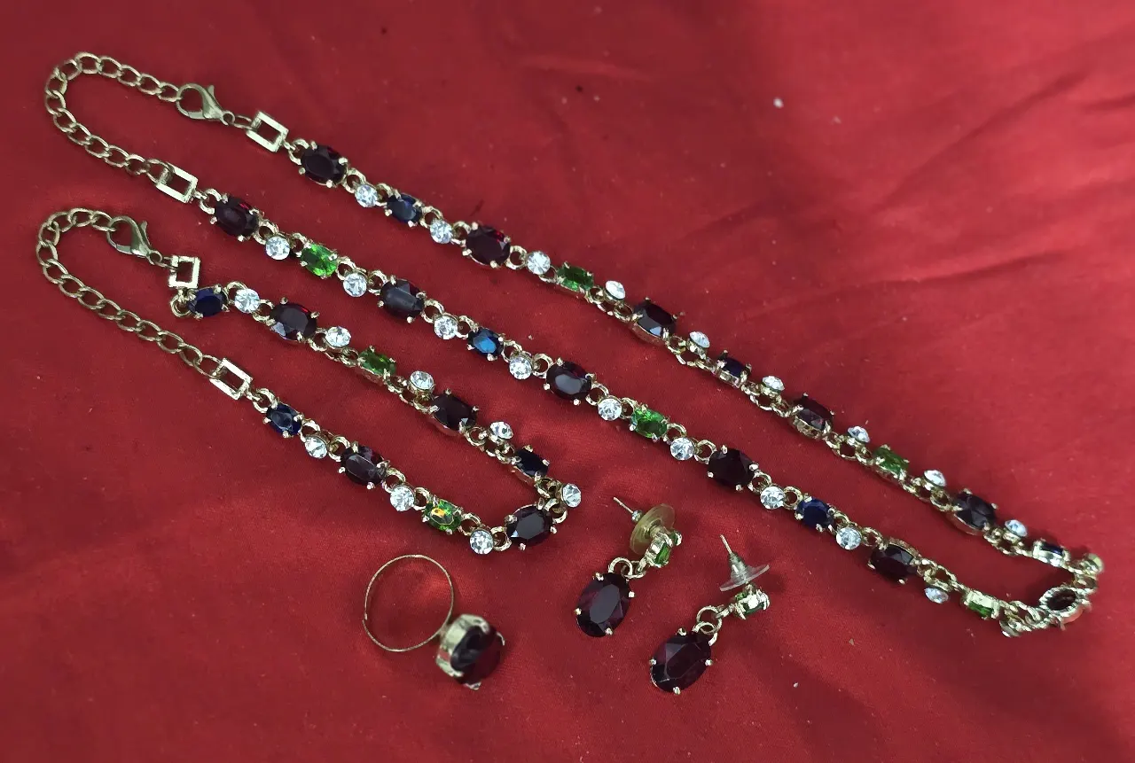 סט תכשיטים תואם בעל מראה קלאסי הכולל ארבעה פריטים 1- שרשרת ארוכה המורכבת מחוליות משובצות אבנים צבעוניות 2- צמיד תואם בעיצובו לשרשרת 3- עגילים זוג עגילי תליון 4- טבעת עם אבן מרכזית גדולה ובולטת האבנים בתחשיט הם רובי אמרלד גארנט ספיר קריסטלים וזרקונים המתכת ציפוי זהב