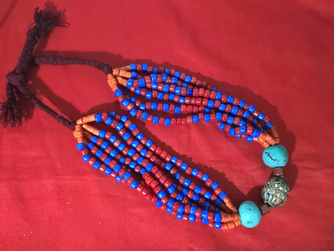 שרשרת תכשיט מרשים בסגנון אתני טיבט נפאל או צפון אפריקה השרשרת מורכבת מריבוי שורות של חרוזים קטנים בצבע אדום וכחול עזים חרוזי טורכיז בחלק התחתון