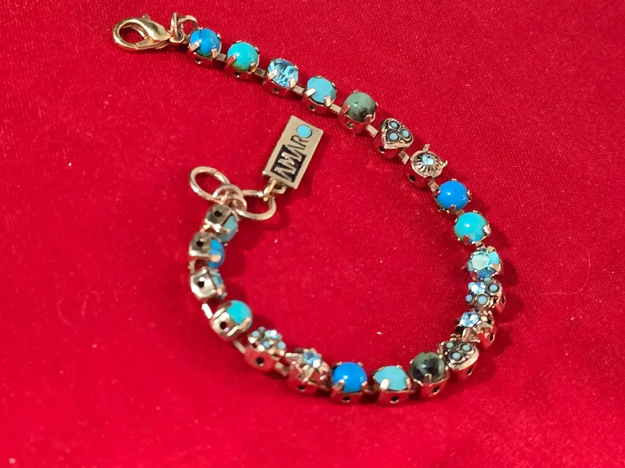 צמיד טניס וינט'ג של המותג אמארו (Amaro) עשוי מפליז בגימור מוזהב ומשובץ באבני תורכיז וקריסטלים בגווני כחול ותכלת