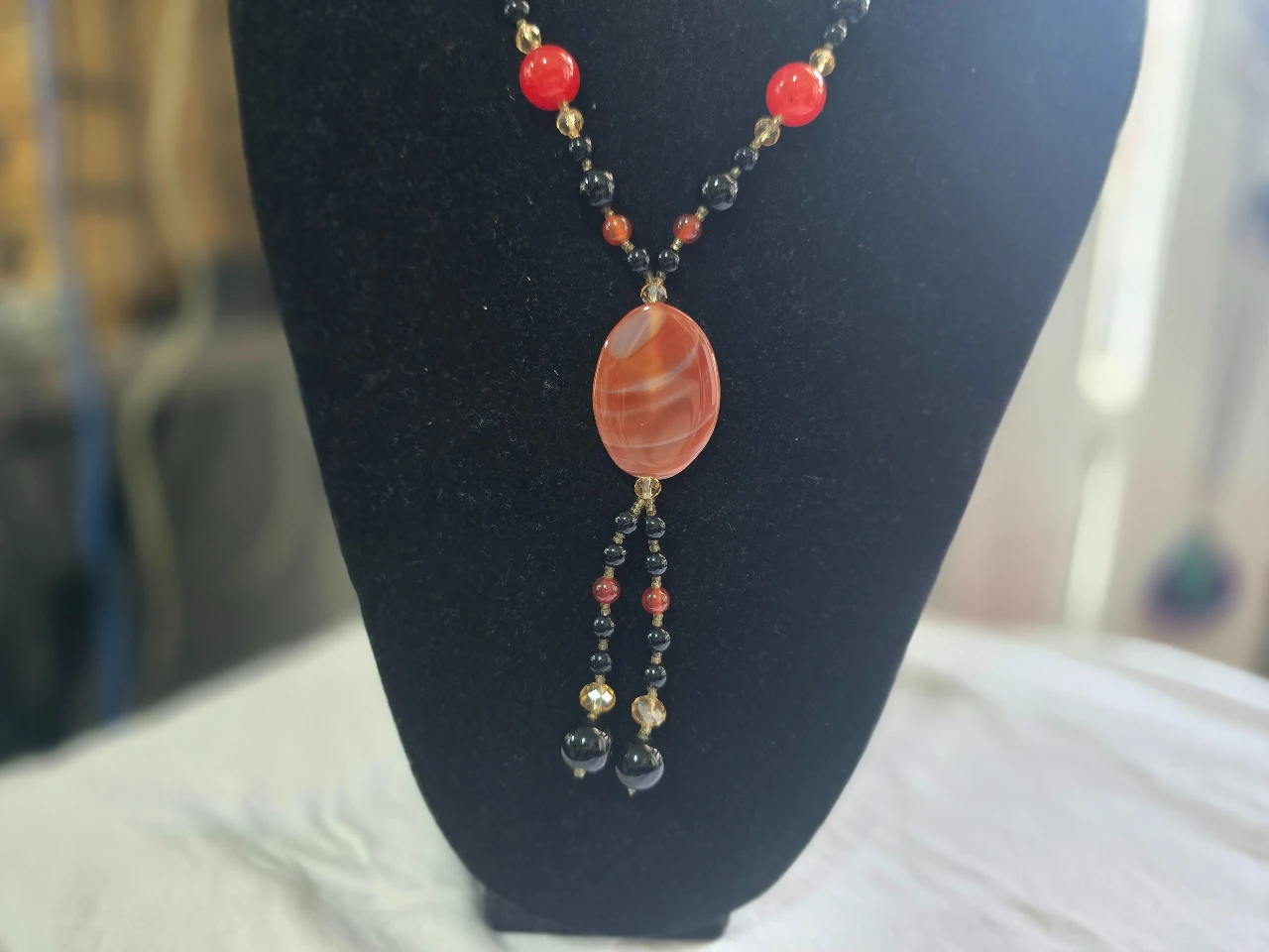 שרשרת ארוכה הכוללת תליון אבן מרכזי השרשרת משלבת אבני קרנליאן כתומות ואדומות עם אבני אוניקס שחורות