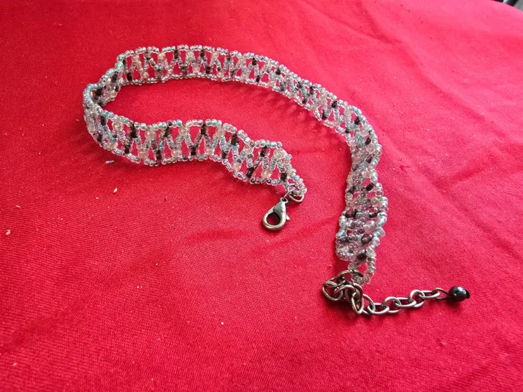 שרשרת בסגנון צ'וקר (Choker) או שרשרת קולר עשויה בעבודת יד חרוזי ונציה קטנים בגוון לבן שחור ואדום התכשיט מאופיין בדוגמת אריגה