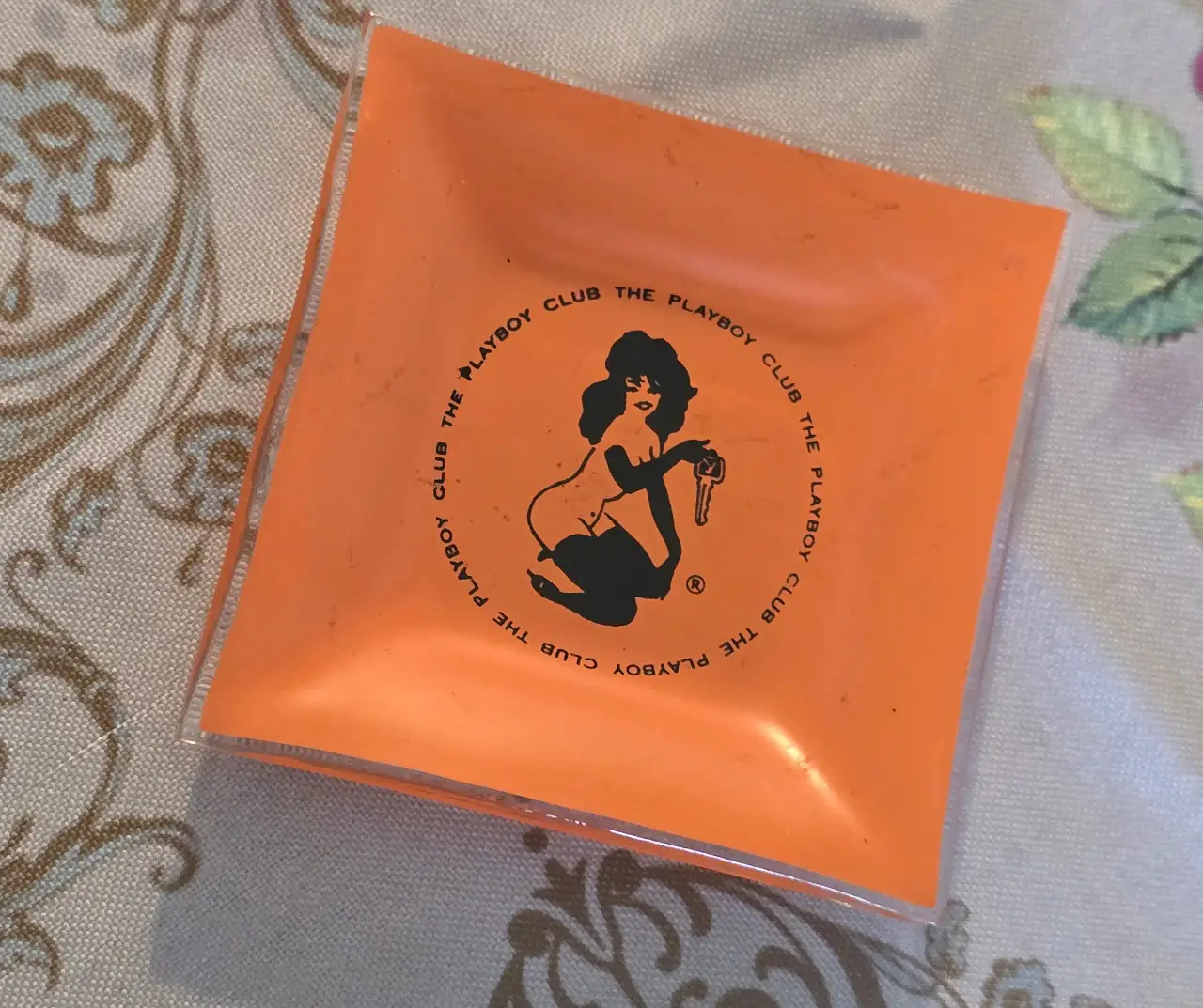 מאפרת זכוכית כתומה וינטג' "The Playboy Club", הדפס דמות ארנבונת המחזיקה מפתח – פריט אספנות רטרו מידות: 9.5 x 9.5 ס"מ