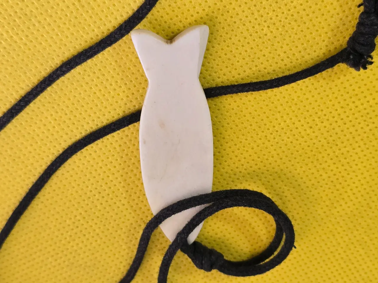 תליון דג נגד עין הרע, מגולף מעצם טבעית בעבודת יד, עם חוט שחור עבה.   מידות התליון - 5.5X1.8 סמ