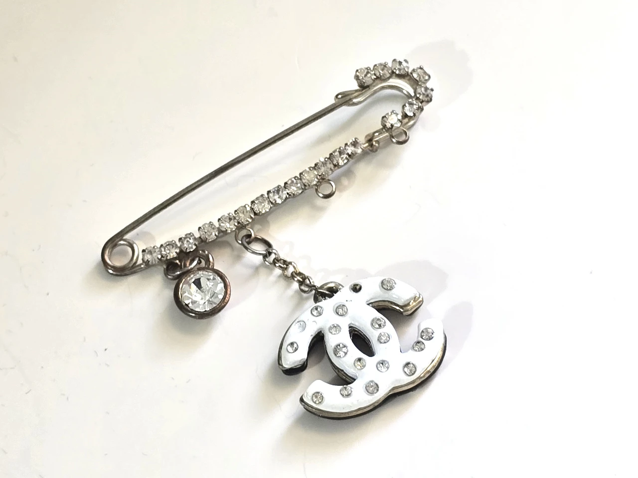 סיכה זו היא סיכת ביטחון שהיא גם סיכת דש כוללת את הלוגו ..שאנל...שמשתלשל ומעוטר בשורת אבני חן קטנות ומנצנצות