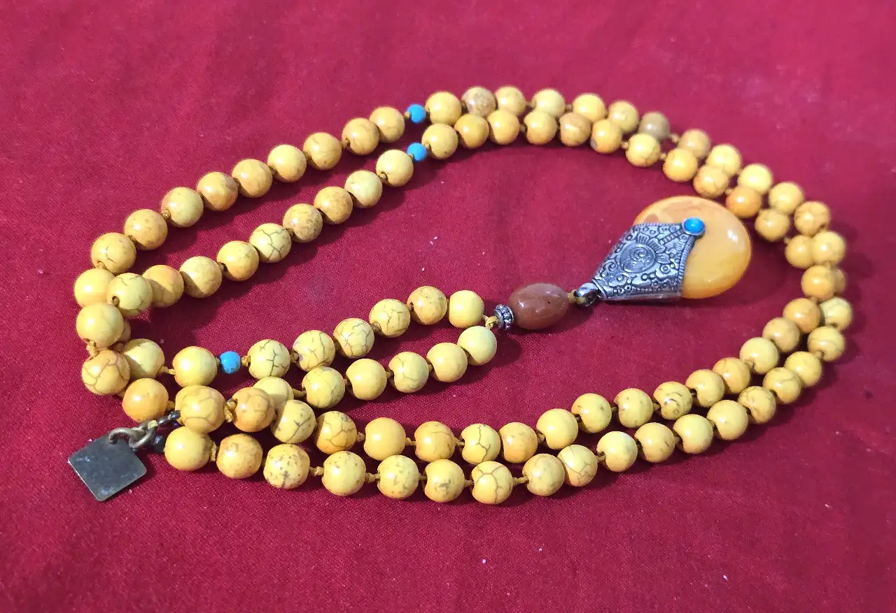 שרשרת חרוזים צהובה הכוללת 108 חרוזים משמשת בבודהיזים ובהינדונזים לספיר אורך המחרוזת 50 ס'מה לתפילה החרוזים אבן עינבר או חרוזי כורכום כולל גם תליון גדול אם אלמנט של כסף טיבטי