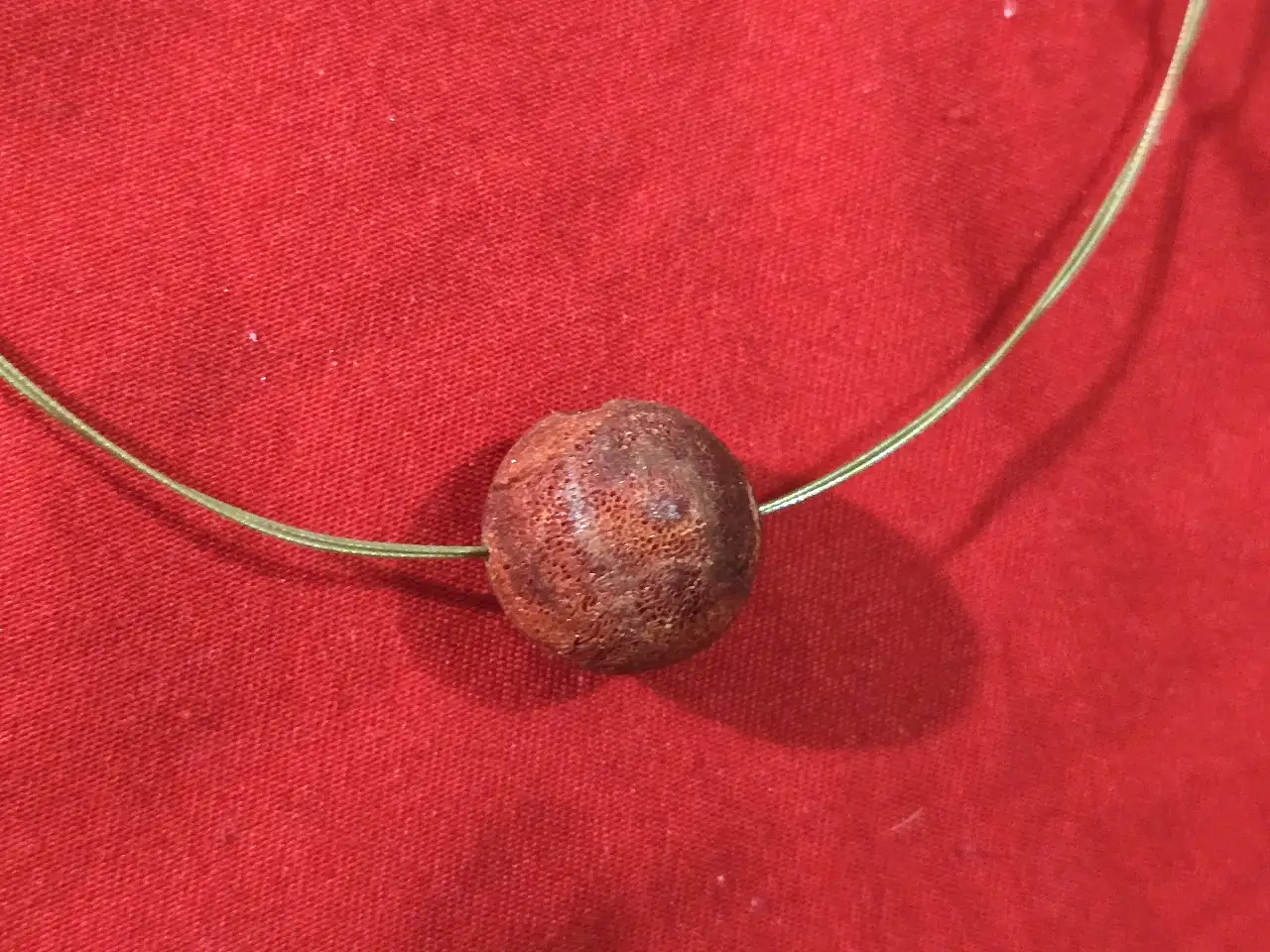 שרשרת קולר בעלת עיצוב מנימליסטי המורכבת מחישוק מתכת דק וחרוז מרכזי בגוון אדום