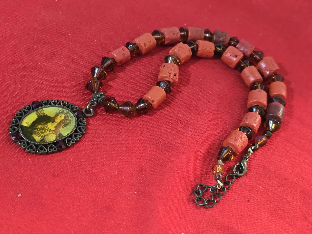 שרשרת בסגנון עתיק עם תליון המציג דמות נסיכה עשויה מחרוזי אלמוג אדומים בצורת גליל וחרוזי גראנט כהים יותר שמפרידים בינהים