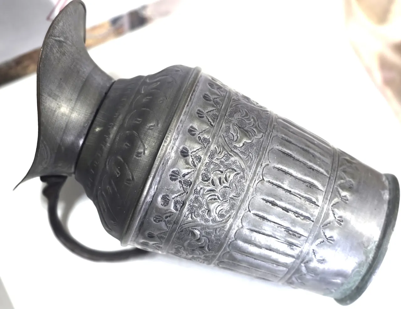 כד נחושת עתיק, מהמאה ה-19, המאופיין בסגנון פרסי או מזרח-תיכוני מסורתי. עשוי נחושת בעבודת יד, (מצופה בדיל) המעניק לו מראה כסוף או אפרפר. הכד מעוטר בדגמים חרוטים (Repoussé) של צמחייה או פרחים, ובעל ידית מעוקלת לנישיאה. גובה 30 סמ