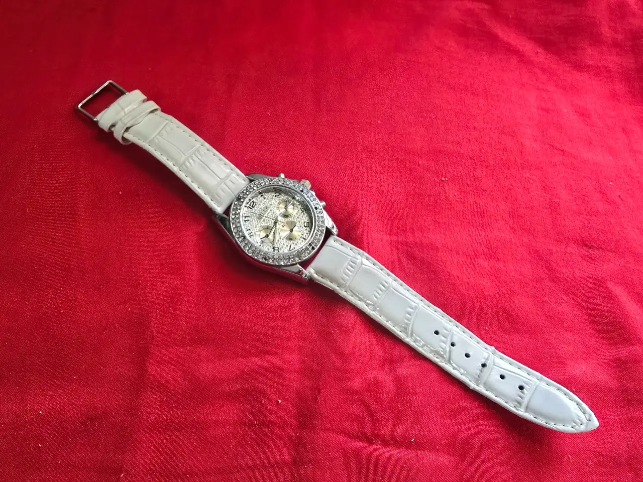 שעון יד חדש לגמרי הלוח מעוטר בשיבוץ צפוף של אבנים קטנות השעון עשוי ממתכת בגוון כסף רצועת עור לבנה דמוי עור תנין