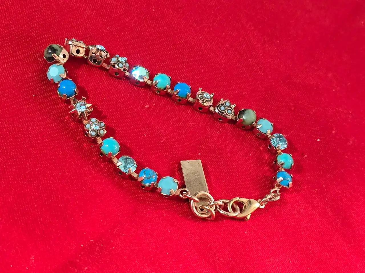 צמיד טניס וינט'ג של המותג אמארו (Amaro) עשוי מפליז בגימור מוזהב ומשובץ באבני תורכיז וקריסטלים בגווני כחול ותכלת