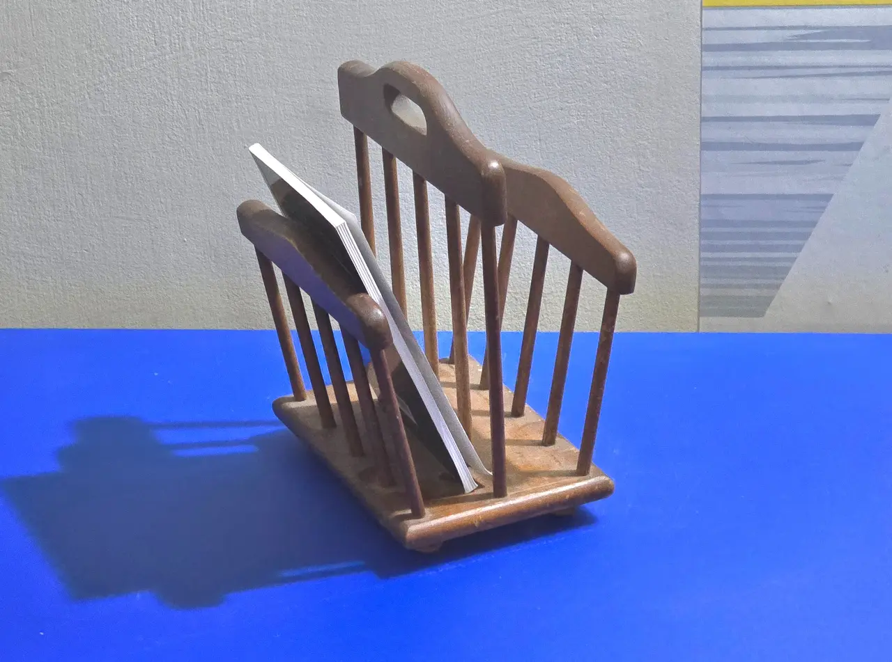 מתקן להנחת ספרי בישול, עשוי עץ בדוגמת מתקן עיתונים, שני תאים וידית. גובה 22 ס"מ. מוט מרכזי מעט מתנדנד.