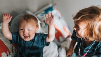 A child looking at their baby sibling laughing
